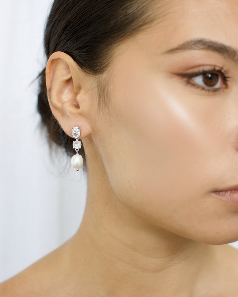 Close-up of a woman wearing pearl earrings with a plain background