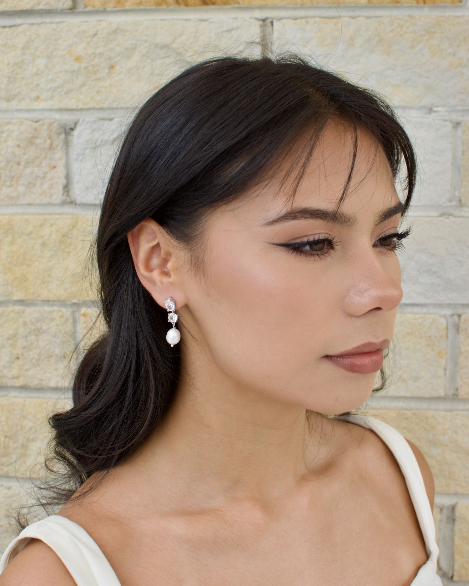 A woman wearing a white dress and earrings with real freshwater pearls and crystal stones.