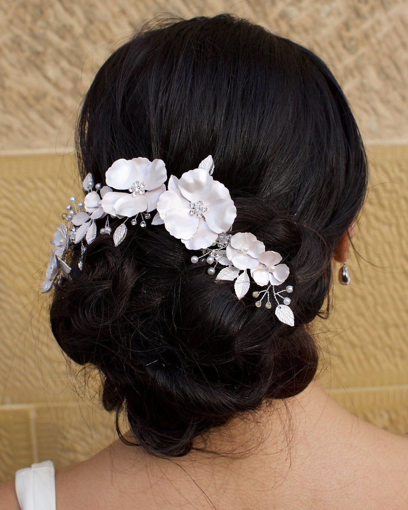 Black haired bride wears a white bridal clip in front of a sandstone wall