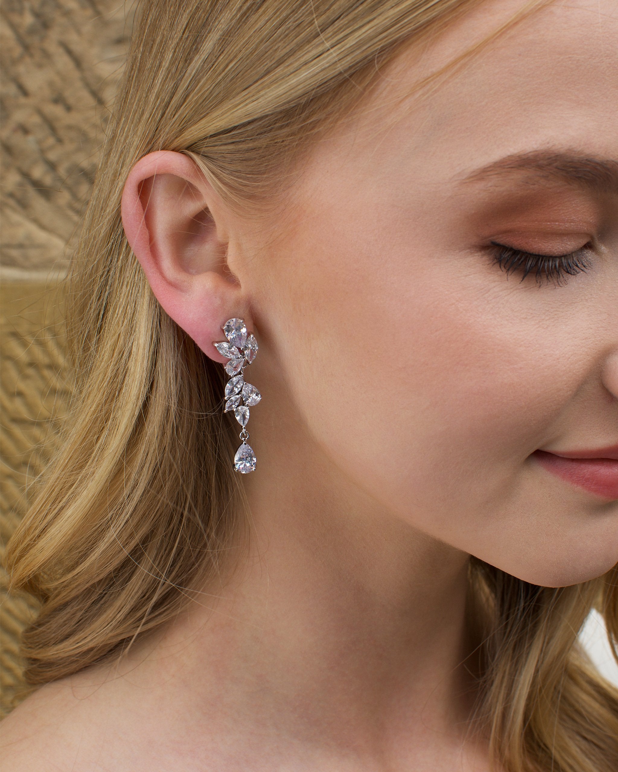 Blonde Model wearing a silver mid length earring with a stone wall backdrop