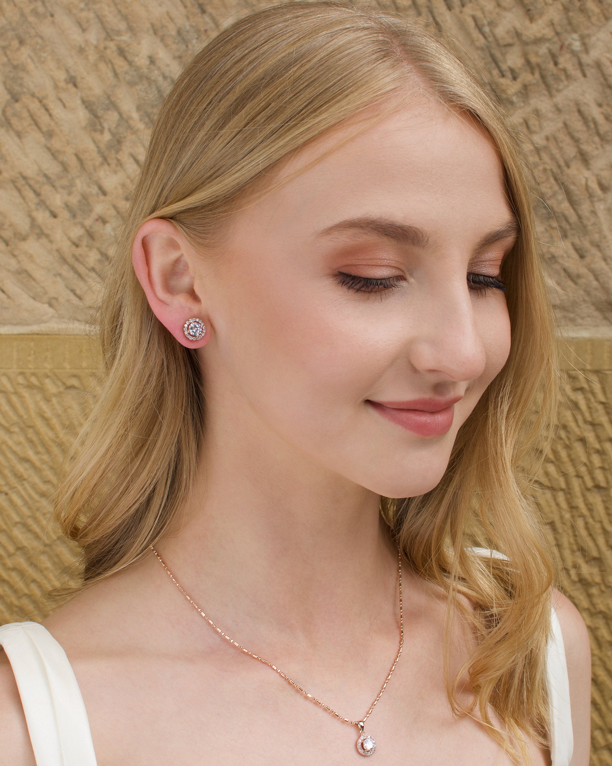 Model wears a simple rose gold chain with a single stone pendant with a stone wall background