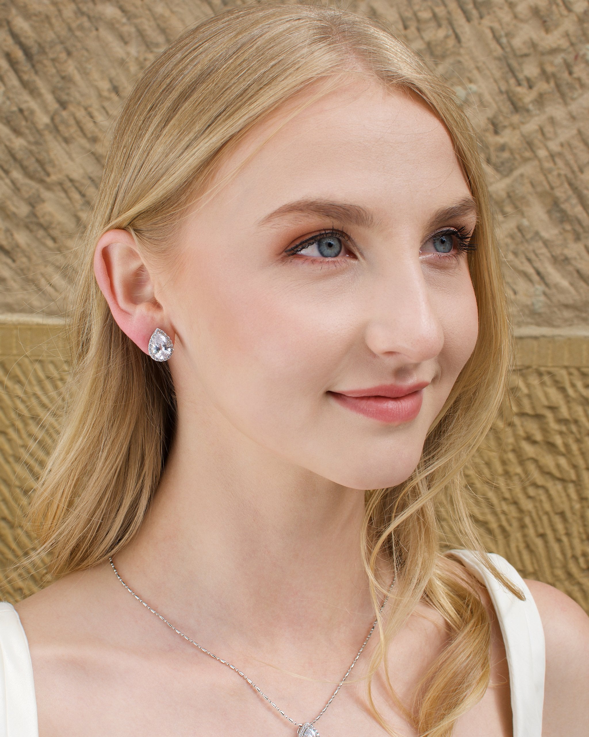 Blonde model wears a crystal teardrop earring and necklace set. A Sandstone wall is the background