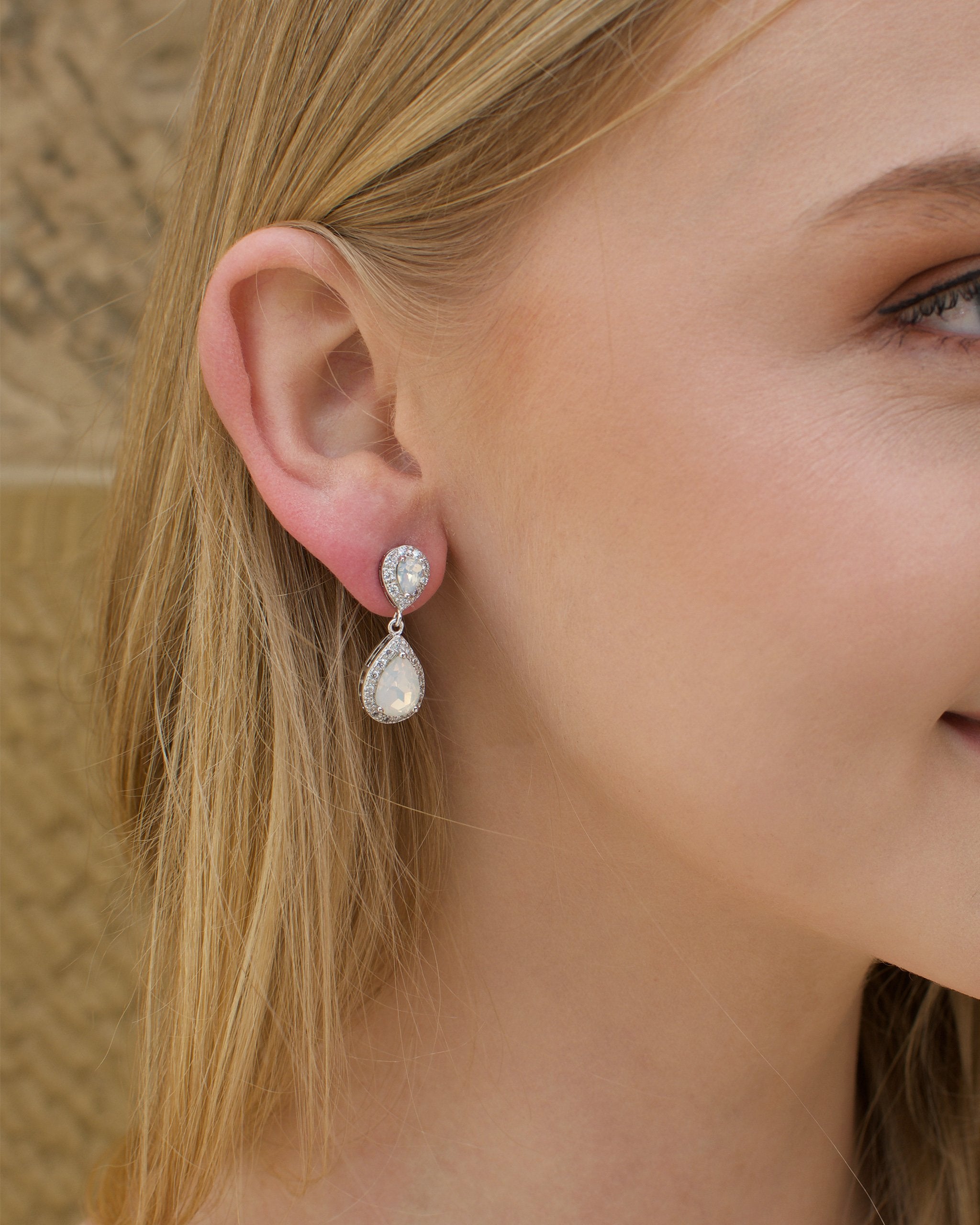 A blonde model bride wears a double teardrop earring with white opal colour stones