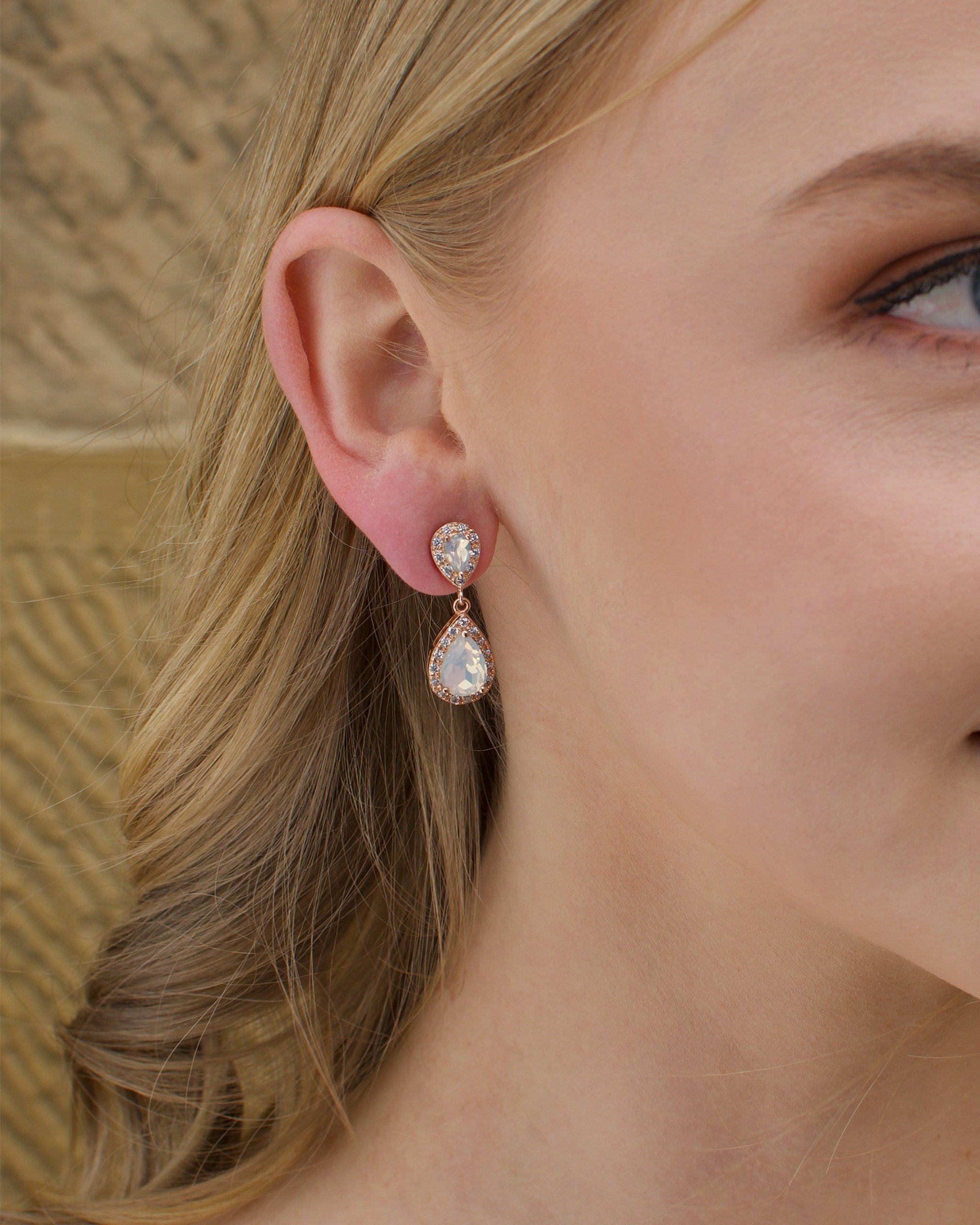 A blonde model bride wears a double teardrop earring with white opal colour stones