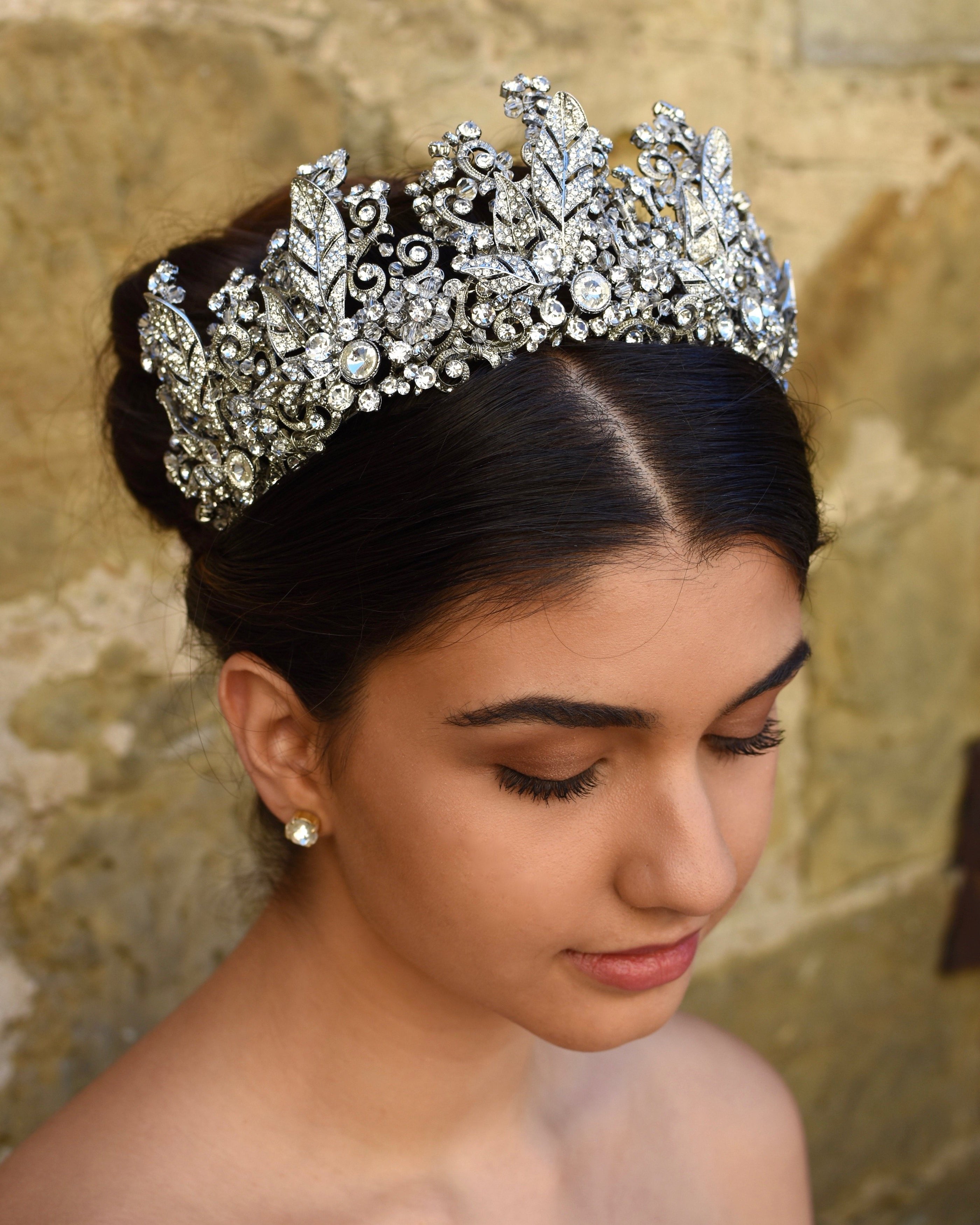 A High Bridal Crown with tall peaks worn by a dark bride with a stone wall backdrop