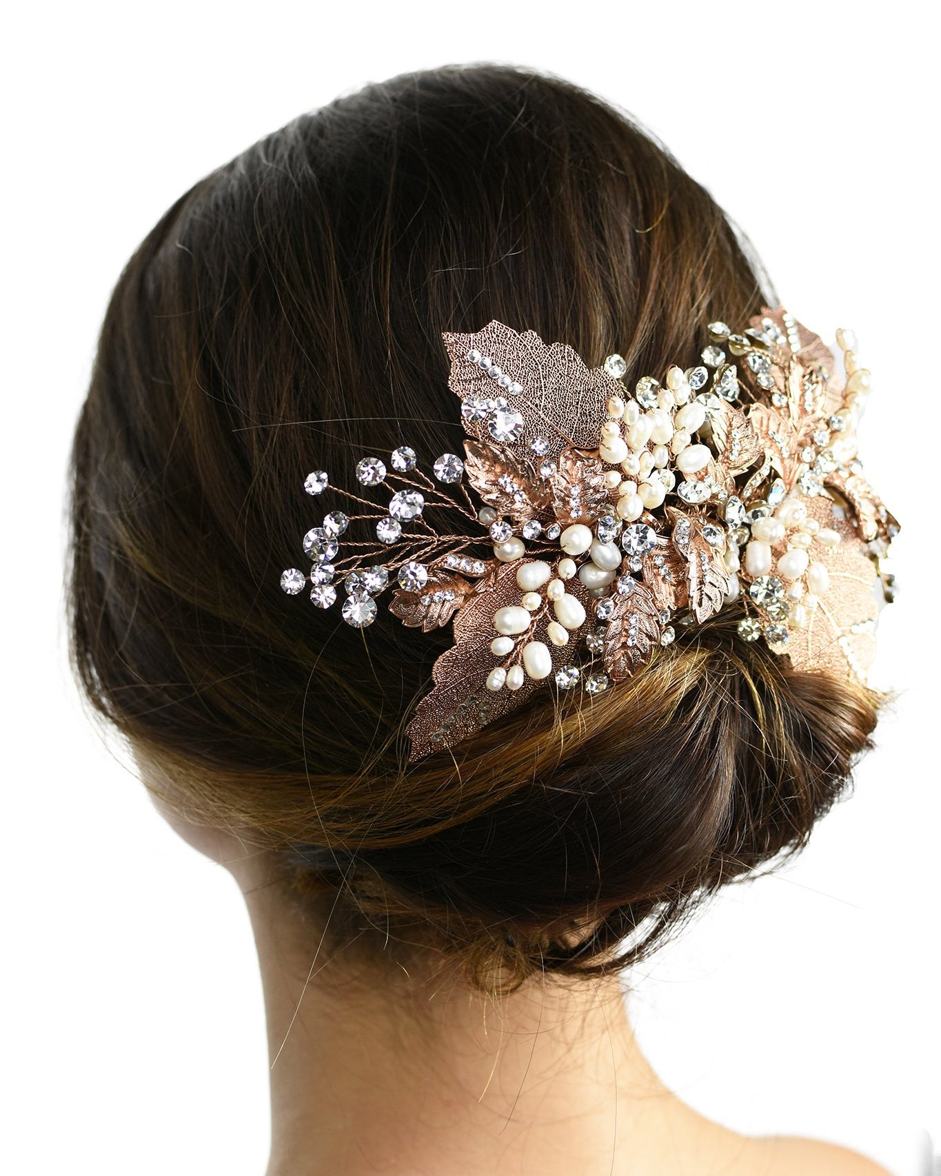 A model with brown hair wears a rose gold and filigree leaves Bridal Vine at the back of her head against a white background