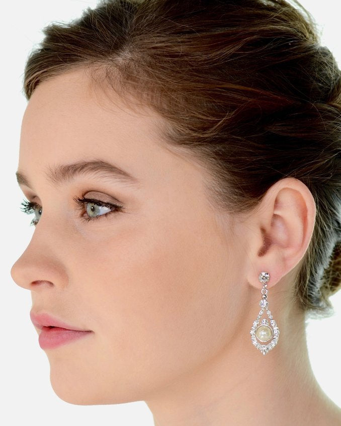 A green eyed model wears a pearl drop earring against a white background