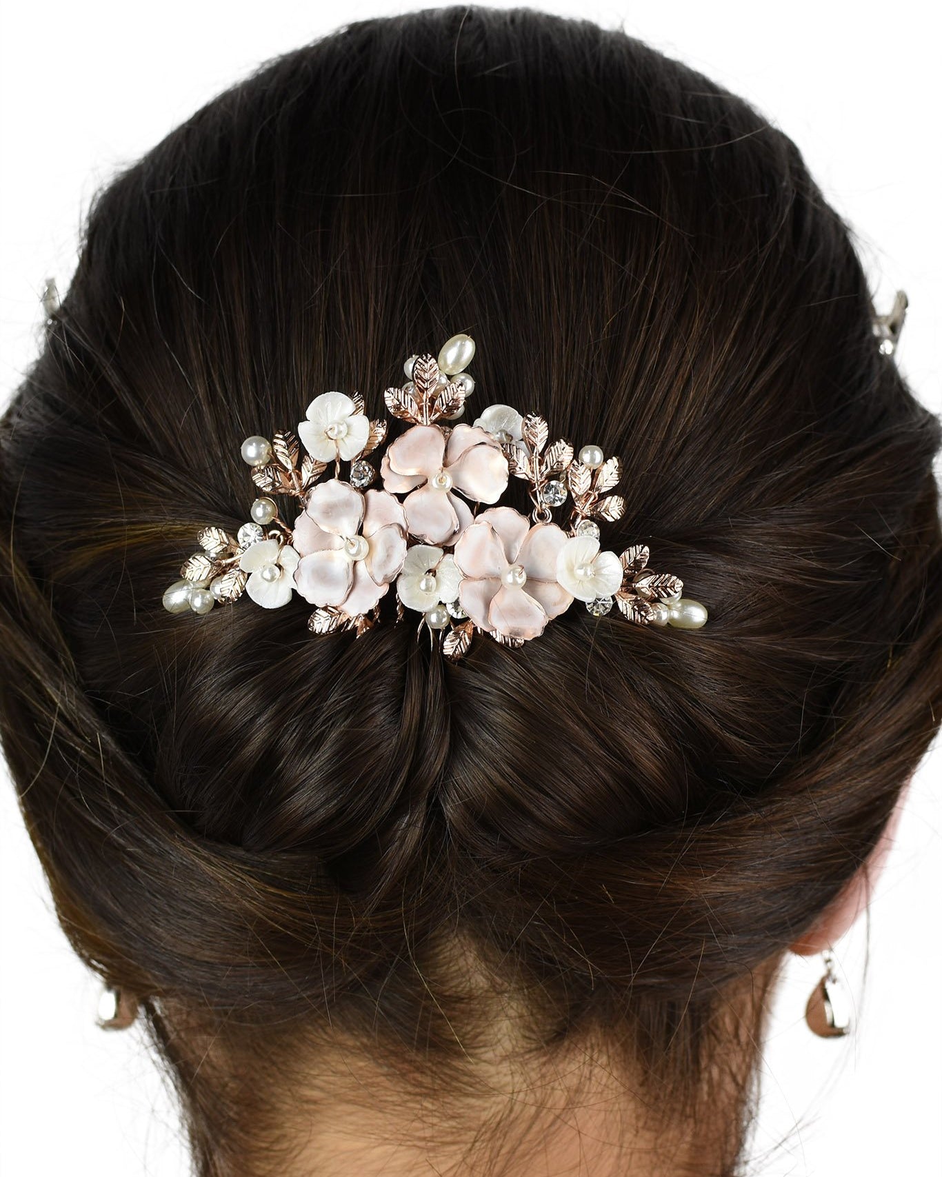 The back of the head of a bride wearing a soft rose gold bridal comb in her dark hair