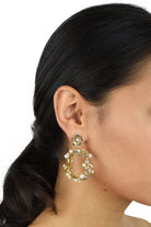 Model wears a gold hoop shape earring. She has dark hair.
