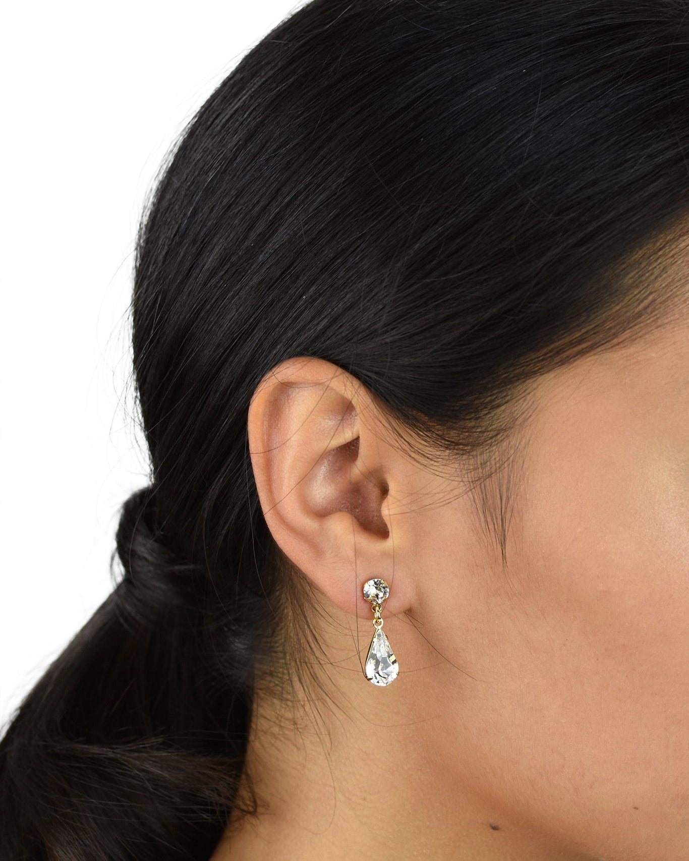 A model wears a simple crystal teardrop earring. She has dark hair