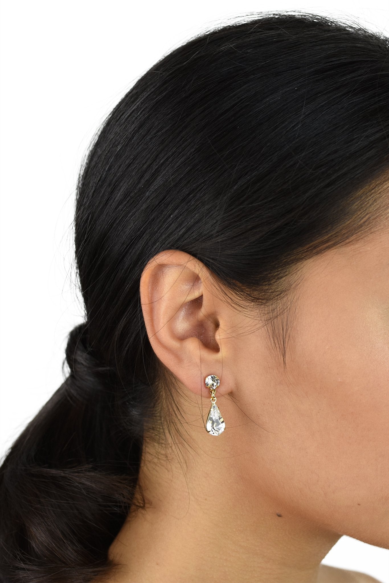 A model wears a simple crystal teardrop earring. She has dark hair