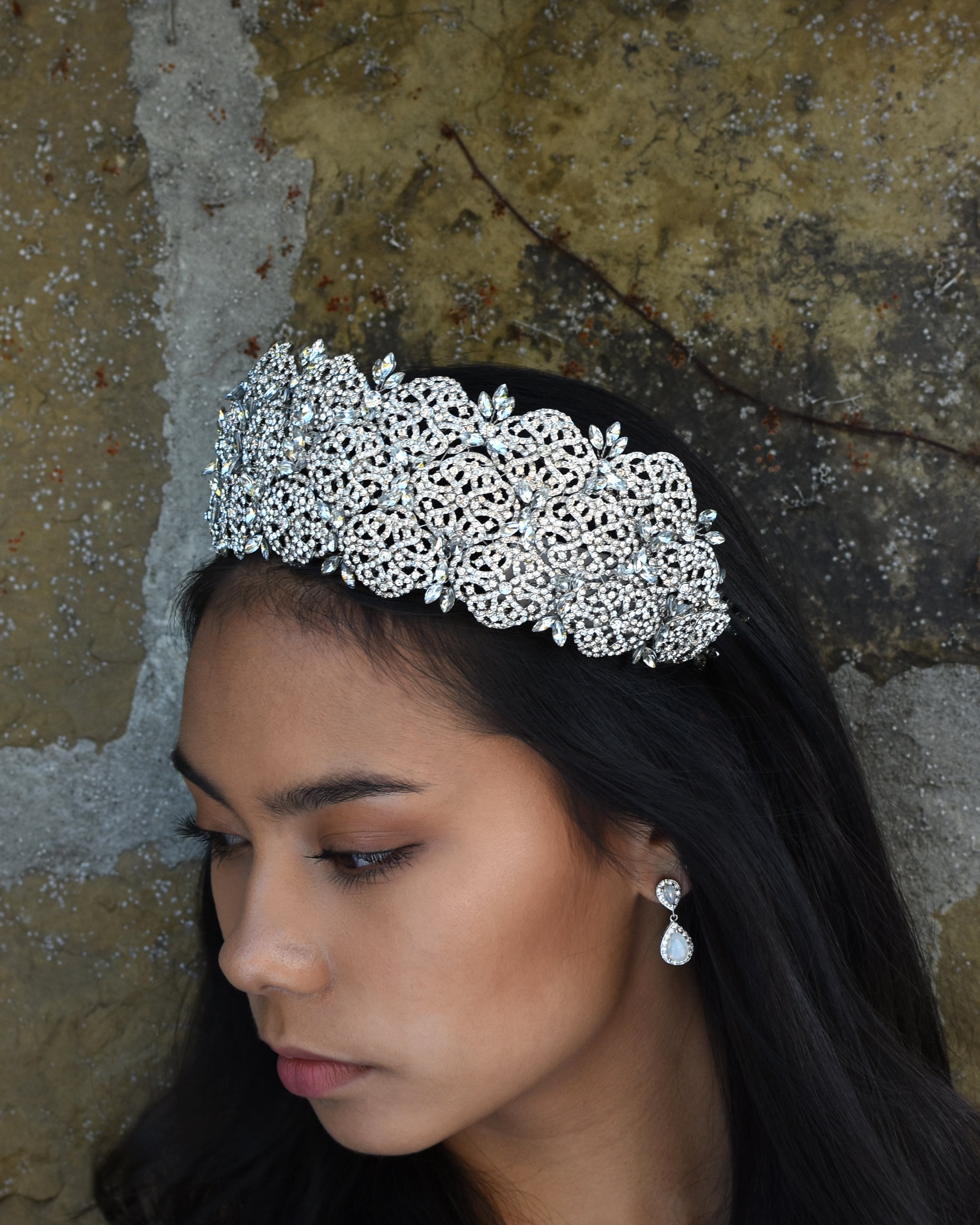 A very high crystal tiara worn by a dark haired bride with a stone wall behind her.