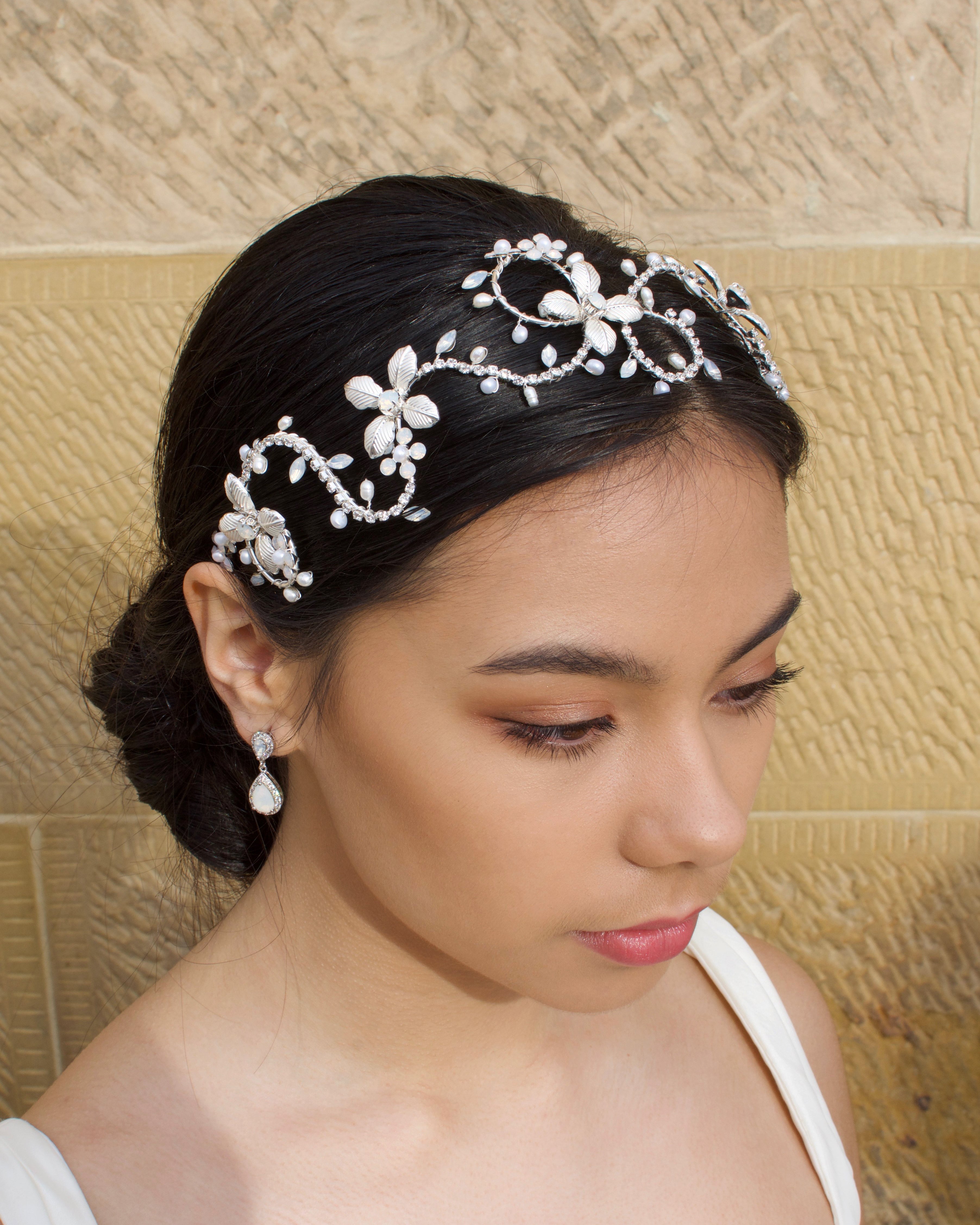 Dark Hair model wears a silver headband with pearls with a stone wall background