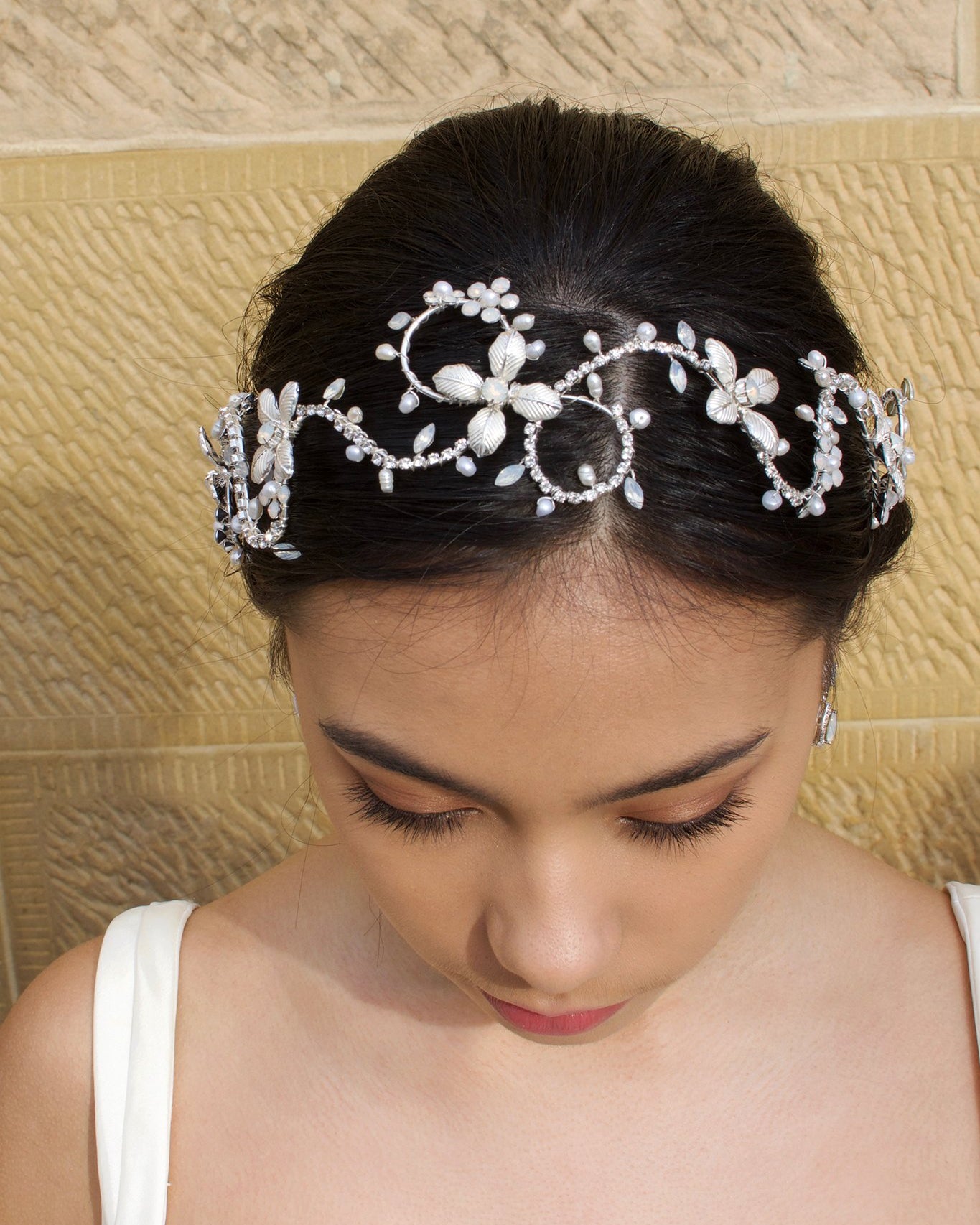 Head down model wears a silver bridal headband with pearls with a stone wall background