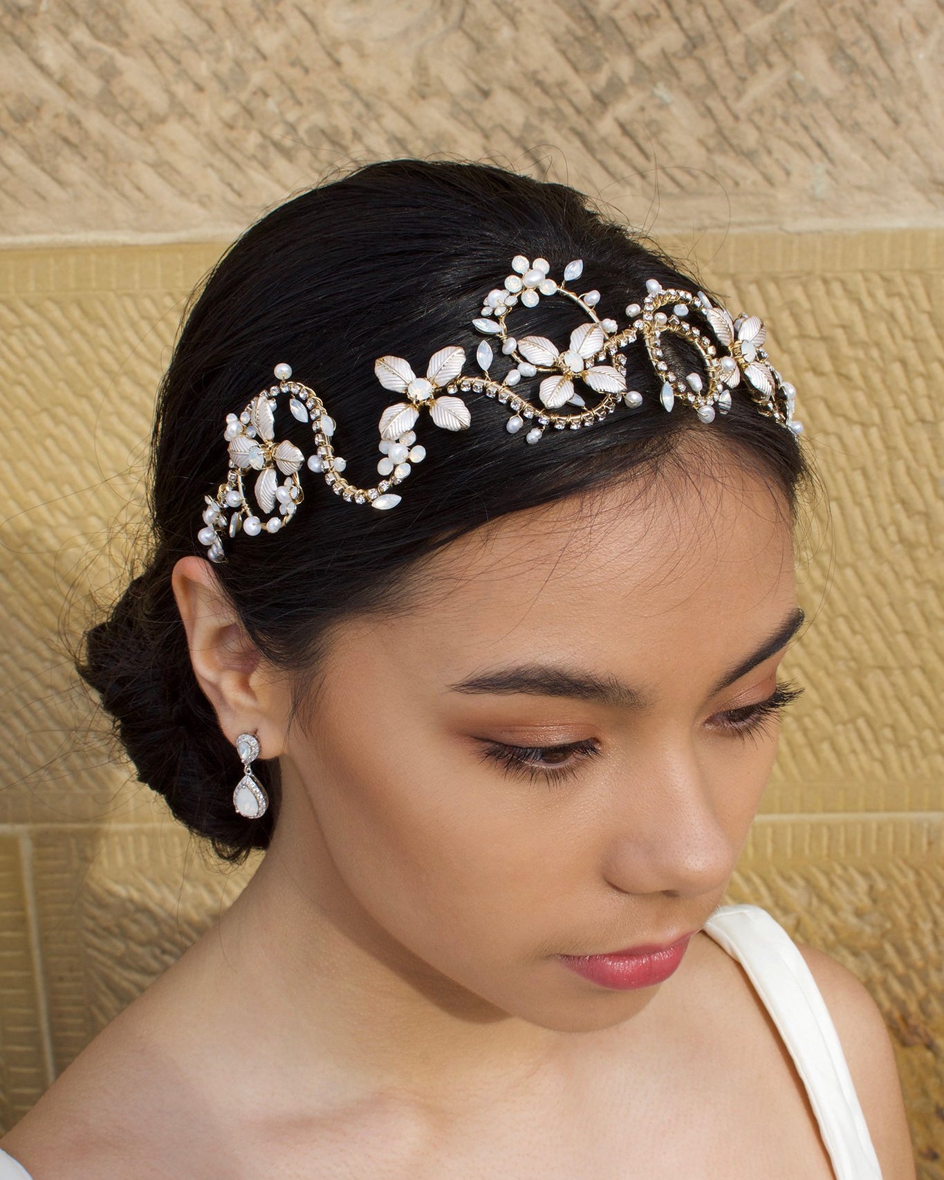 Black hair model wears a gold leaf headband. The model is standing in front of a sandstone wall.
