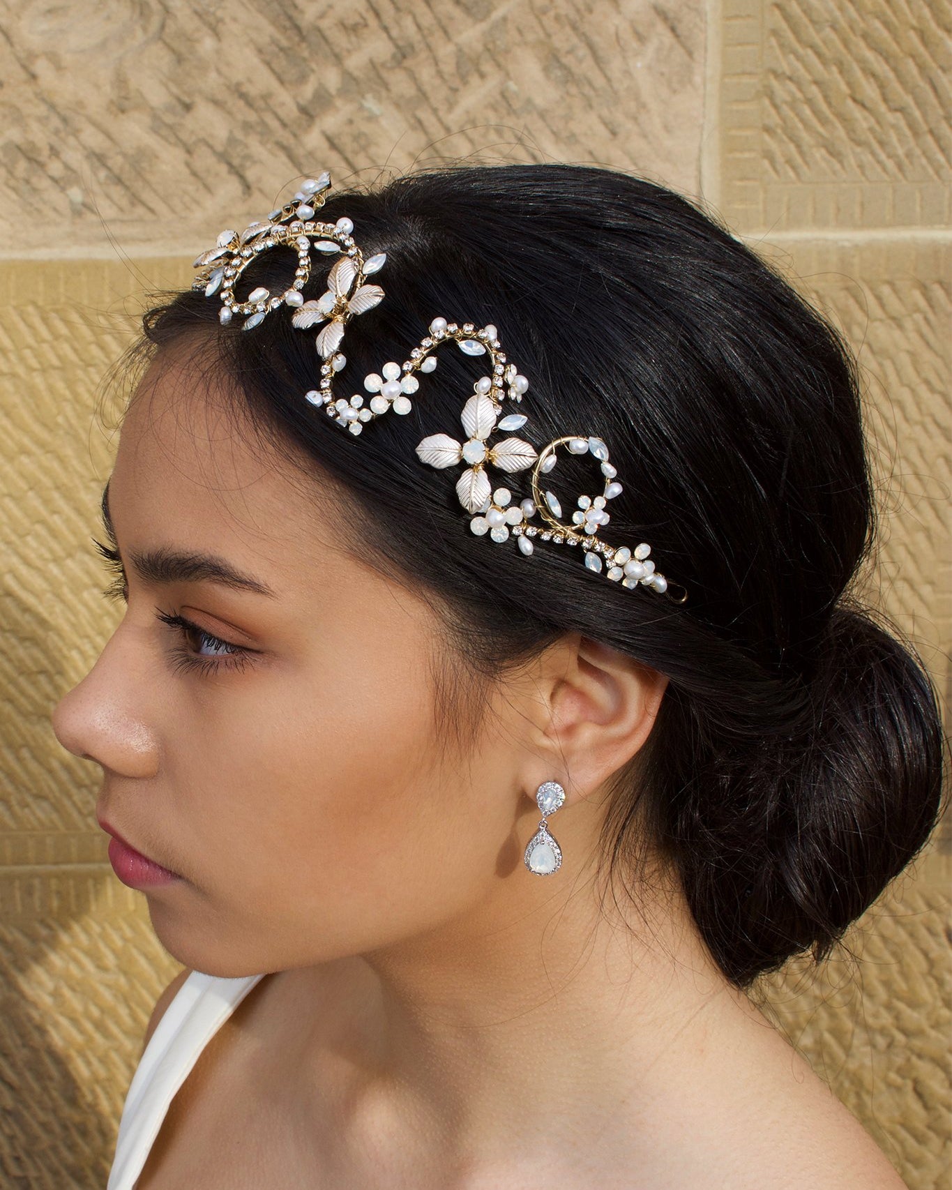 A side view of a model with dark hair wearing a gold bridal headband