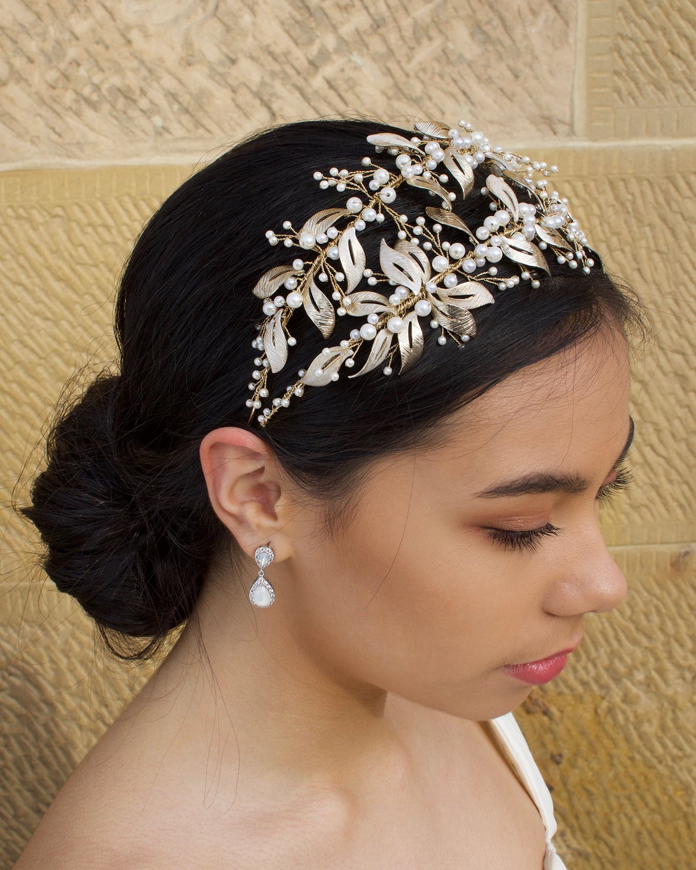 Double row pale gold headband with pearls worn by a dark hair model with a sandstone wall