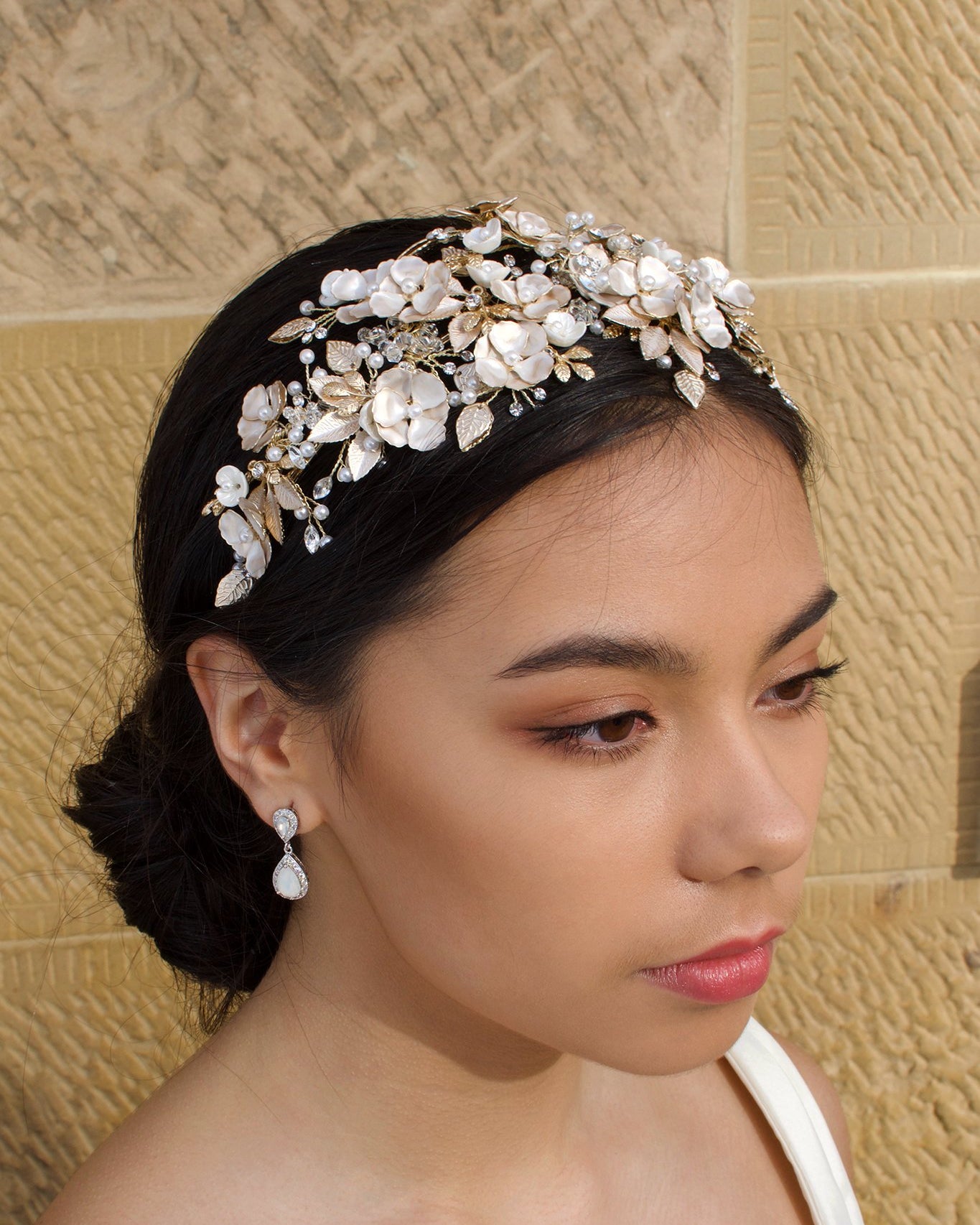 Dark Haired model wears a wide Pale Gold headband of flowers with the background of a stone wall