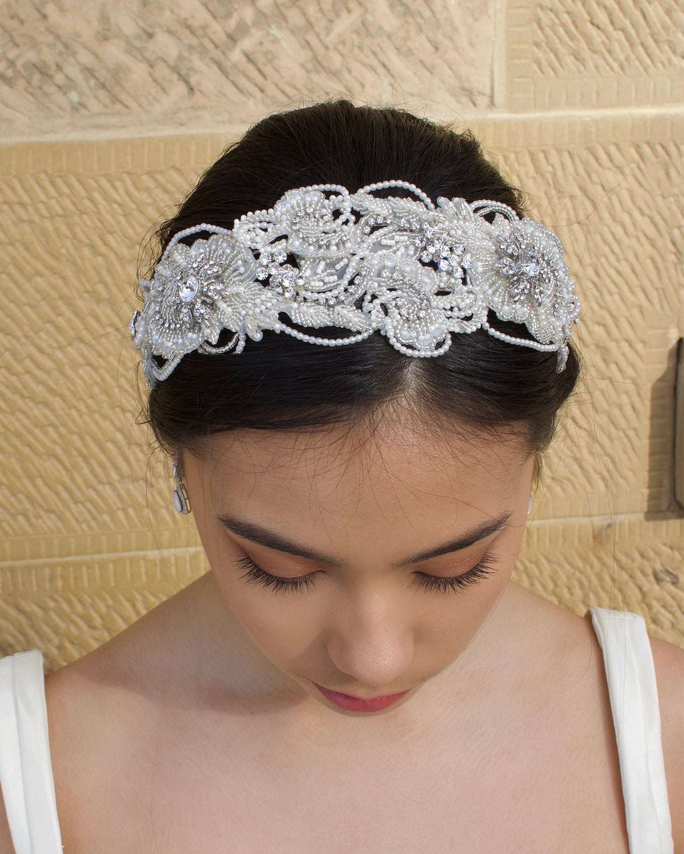 Top View of a dark hair model wearing a seed pearl handmade Bridal Headband with a stone background
