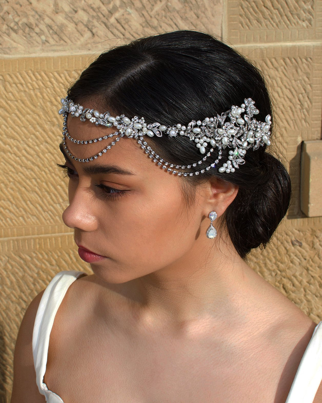 A black haired model wears a bridal vine with loops at the front of the head. With a stone wall background