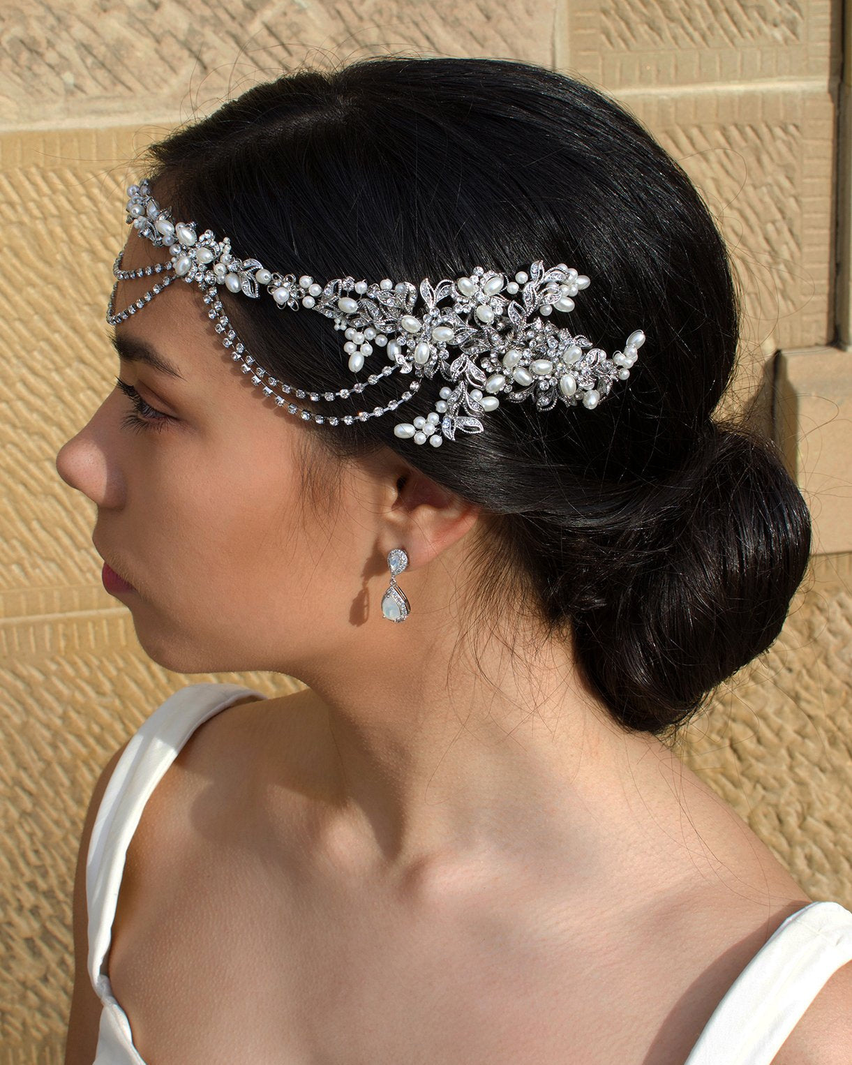 On the side of her head a bride wears a pearls and rhodium handmade vine with a stone wall backdrop