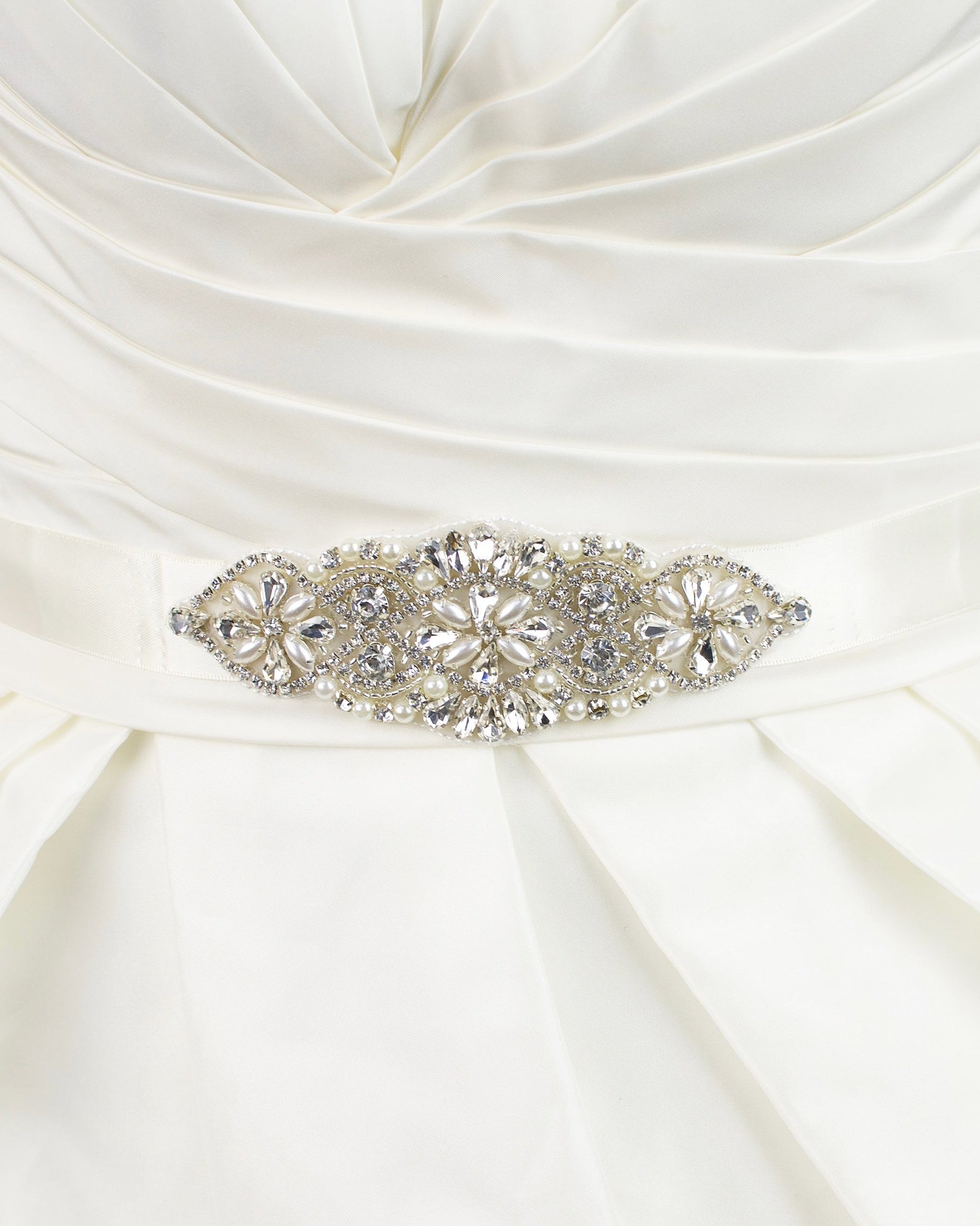 Small crystal and pearl bridal belt motif on an ivory ribbon worn on an ivory dress with white background