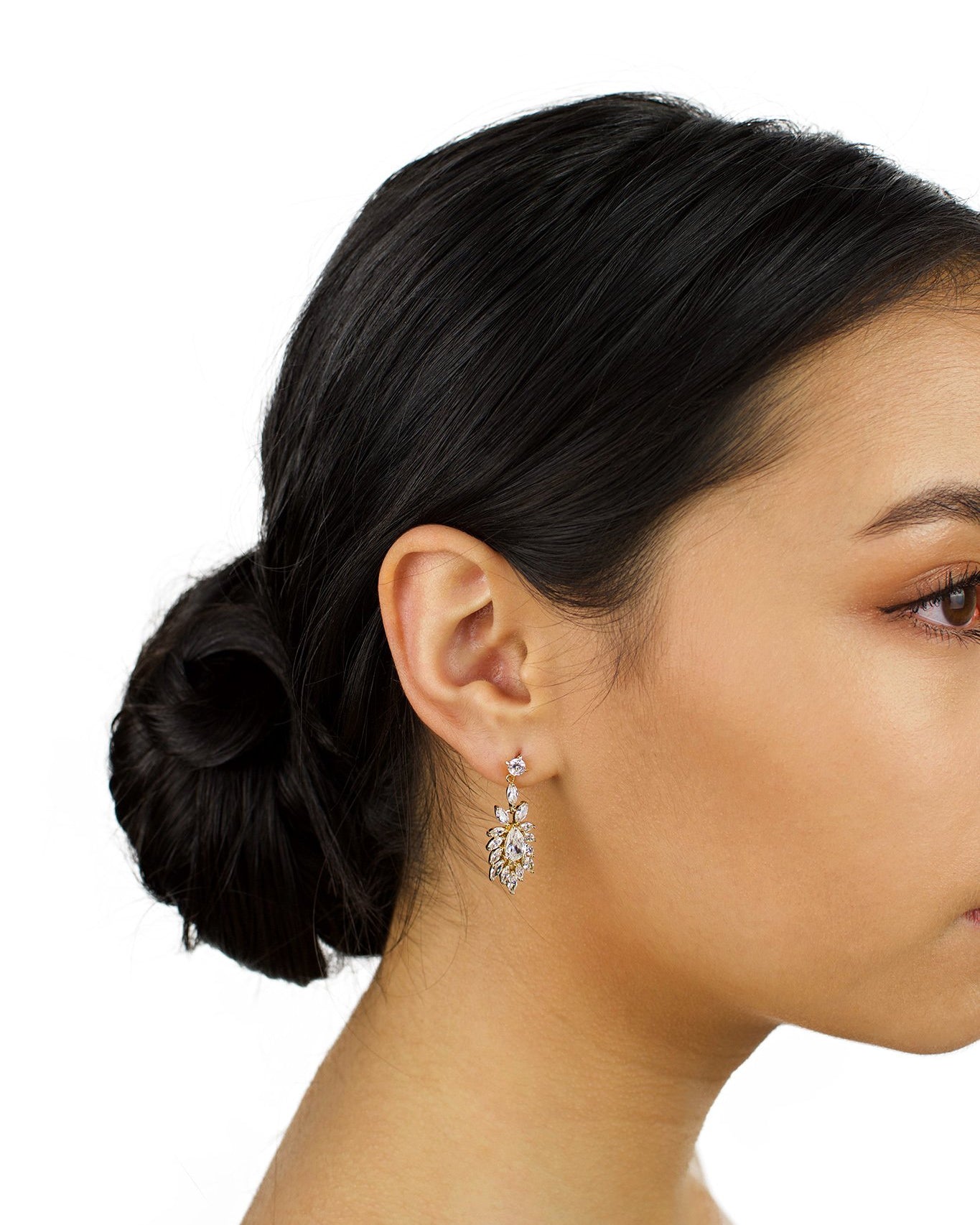 A short drop earring in gold is worn by a dark hair bridal model with a white background