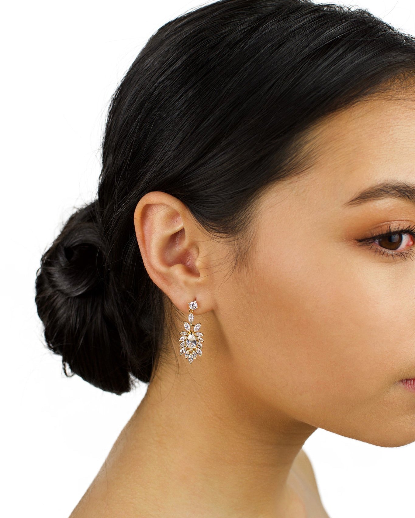 Model wears a gold drop earring in her ear with dark hair and a white background