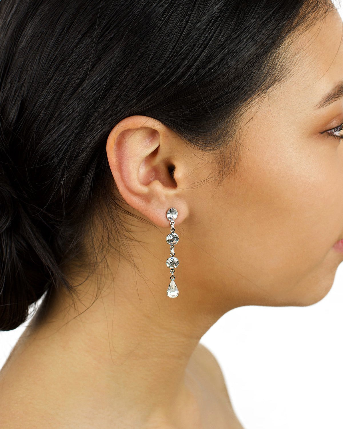 A dark hair model is wearing a long narrow earring in silver with clear stones