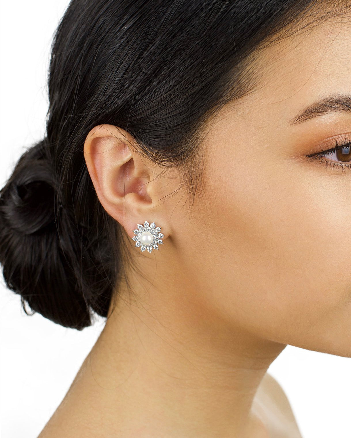 Model with dark hair up wears a stud earring of pearl and crystal with a white background