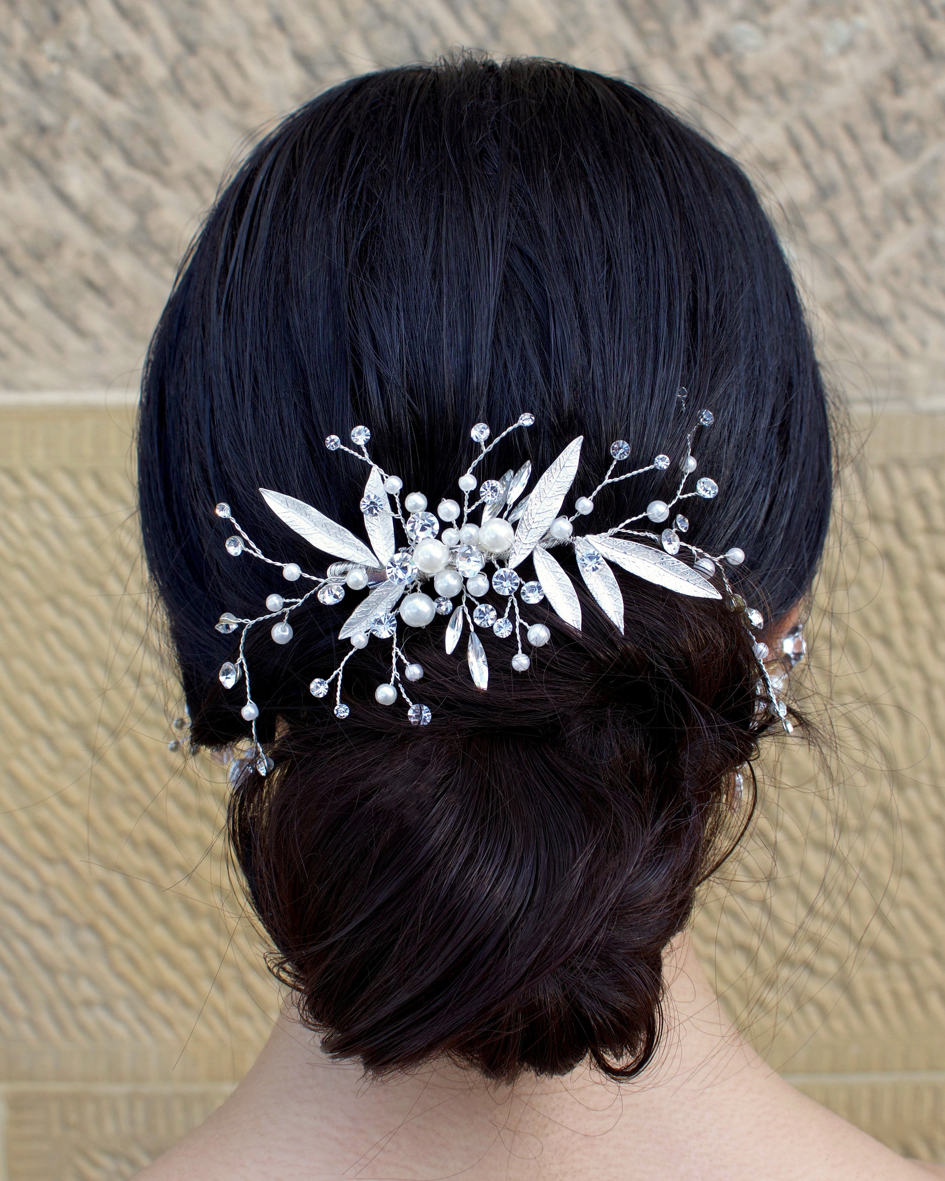 Silver leaf comb at the back of a brides head on dark hair with a stone wall backdrop