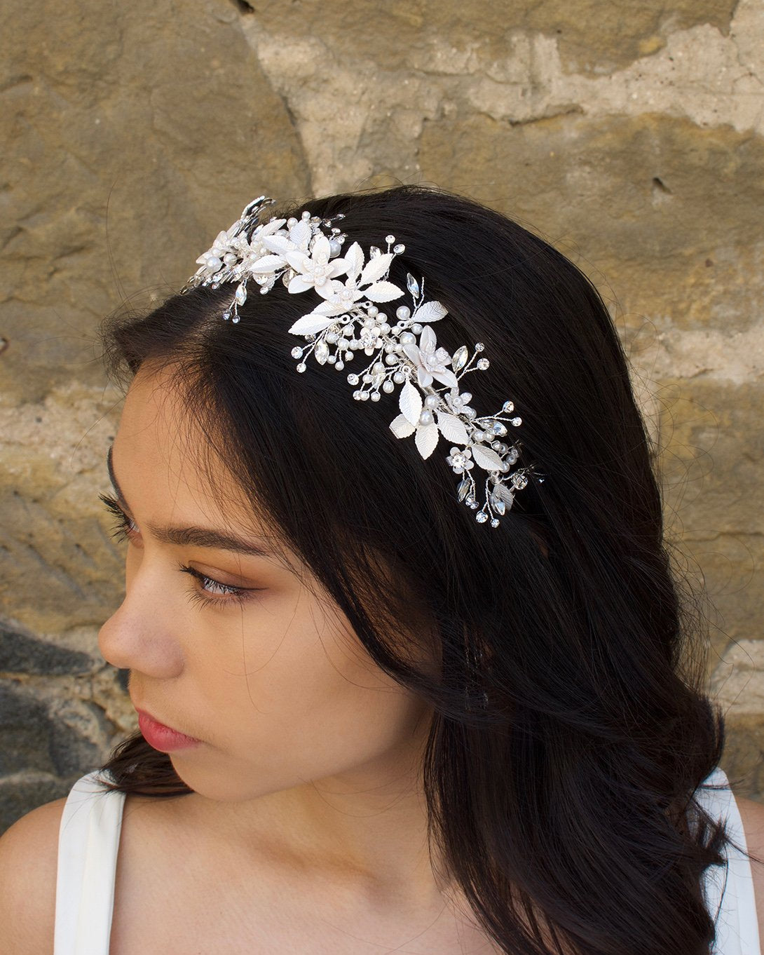 Dark hair bride wears a silver leaves bridal headband with a wall as backdrop