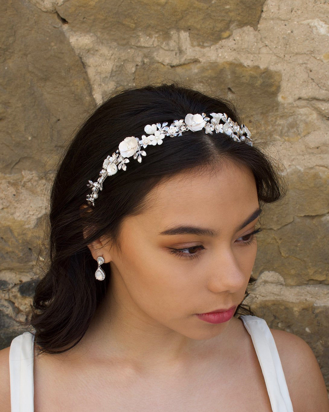 Brown Haired model wearing a ceramic flower headband in silver with a stone wall background