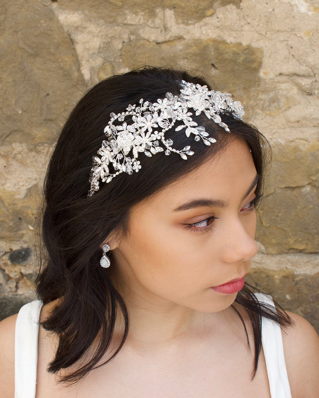 Model wears a silver crystal headband on her dark hair with a stone wall background
