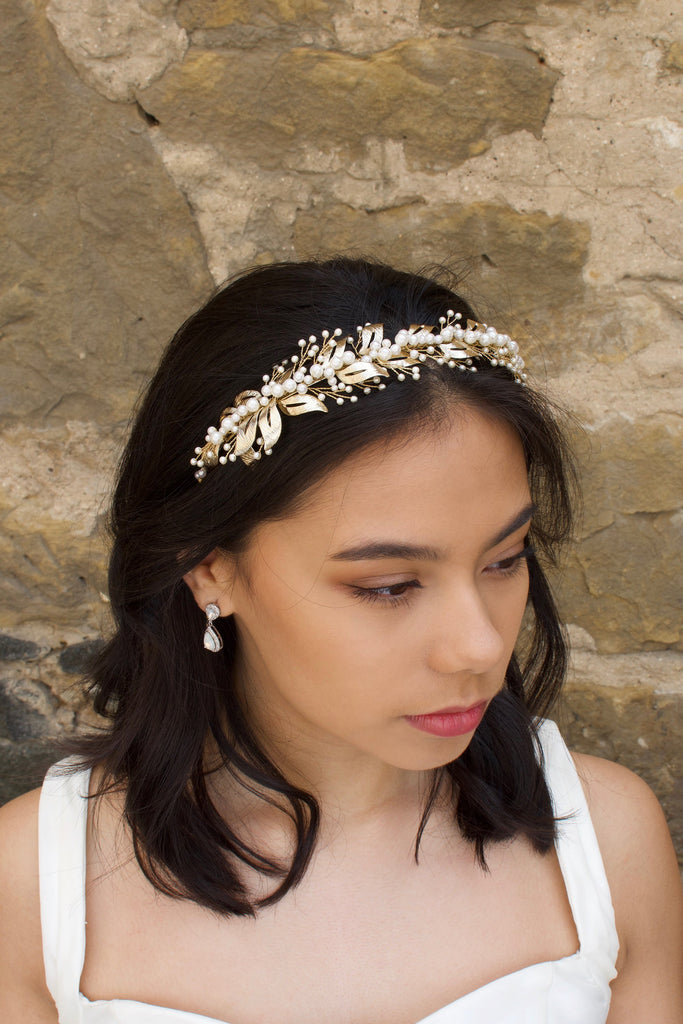 In front of a stone backdrop a dark hair bride wears a headband of pale gold and pearls 