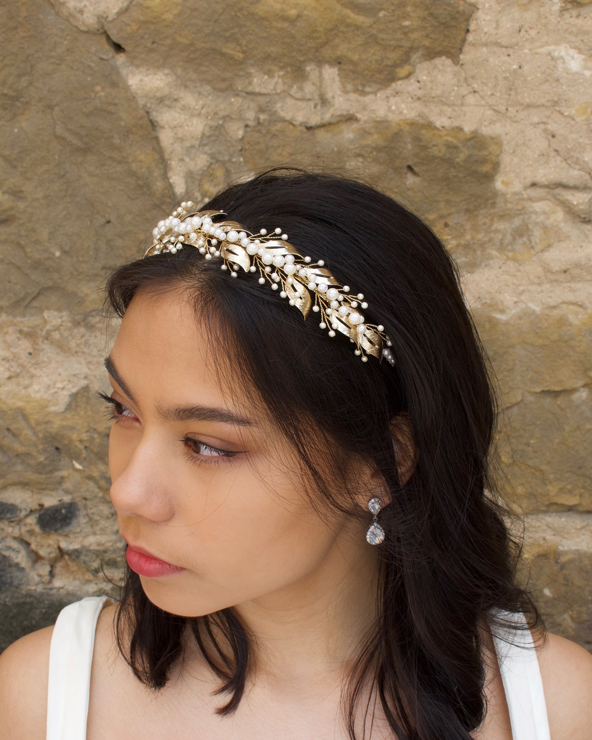 Looking away a model bride wears a pearls and pale gold headband on her dark hair