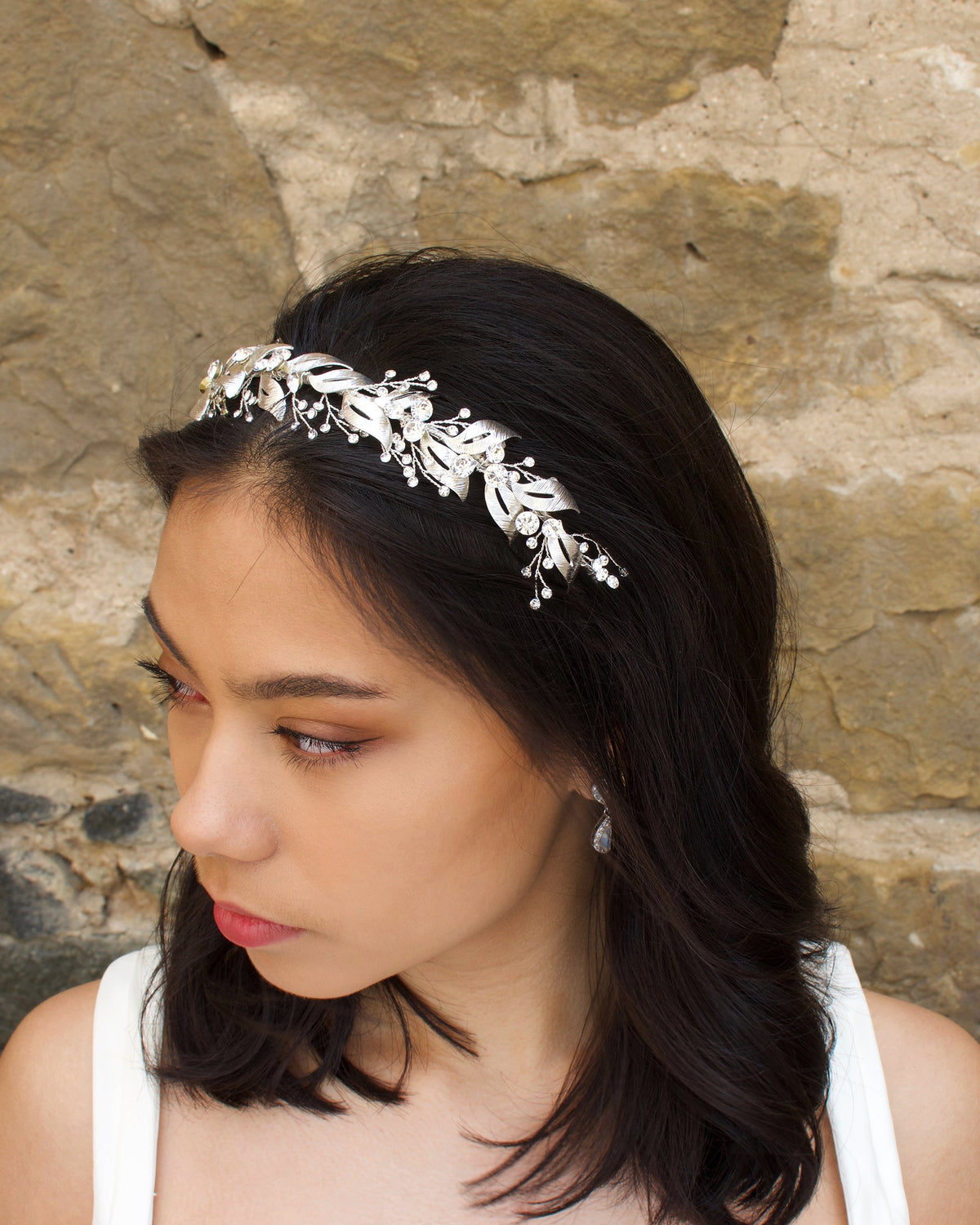 Looking to the left a model wears a beautiful silver bridal headband in her dark hair