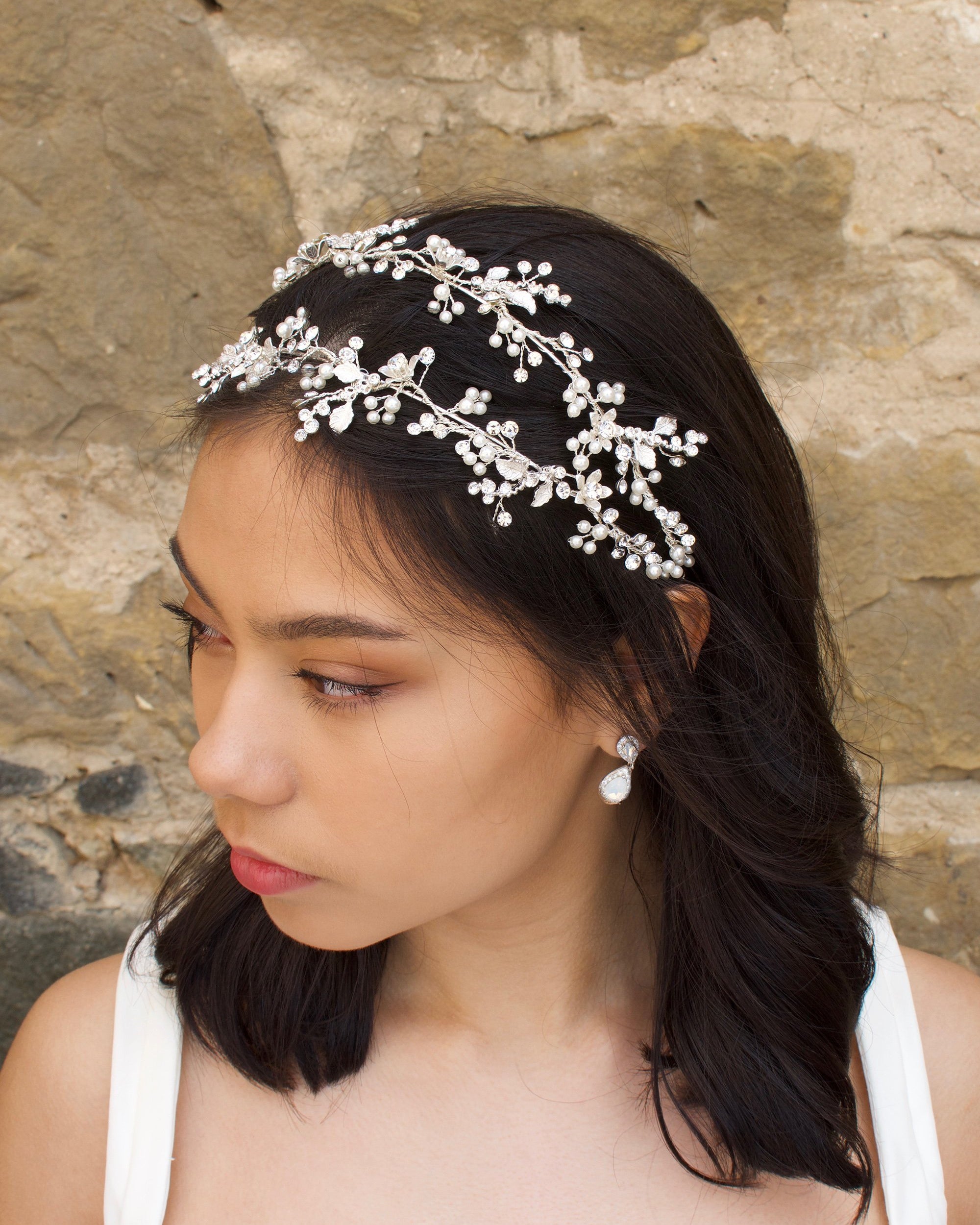 Silver double row headband on a black hair model with a pearl earring and a stone wall backdrop
