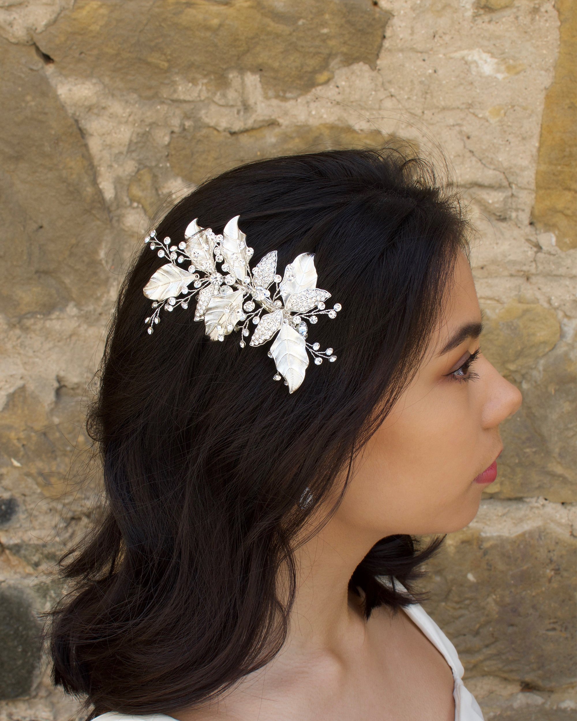 Silver Leaves Side Comb with sprigs of stones worn by a dark hair model with a stone wall backdrop