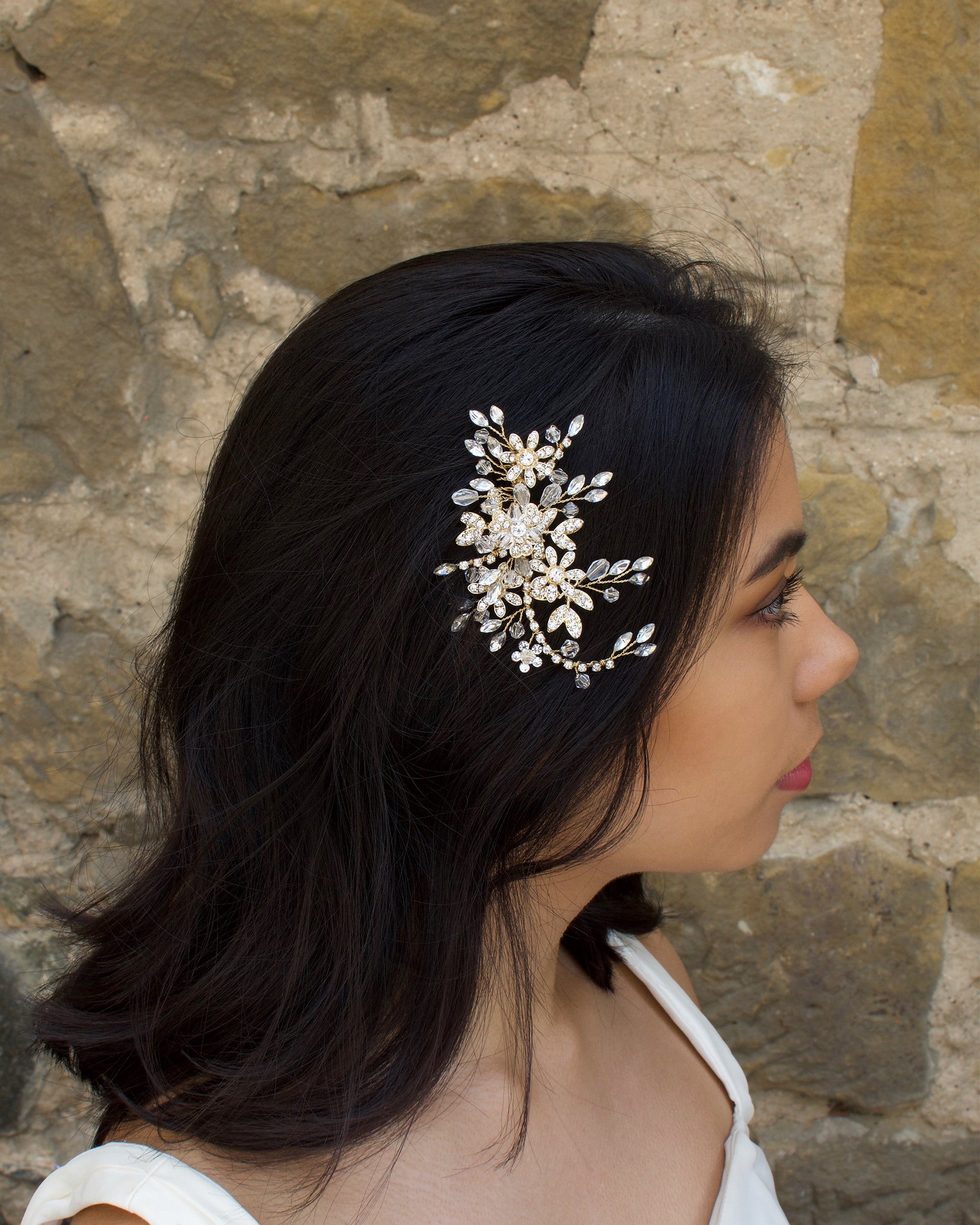 Gold Leaves and Crystals side comb worn by a dark haired model with a stone wall background