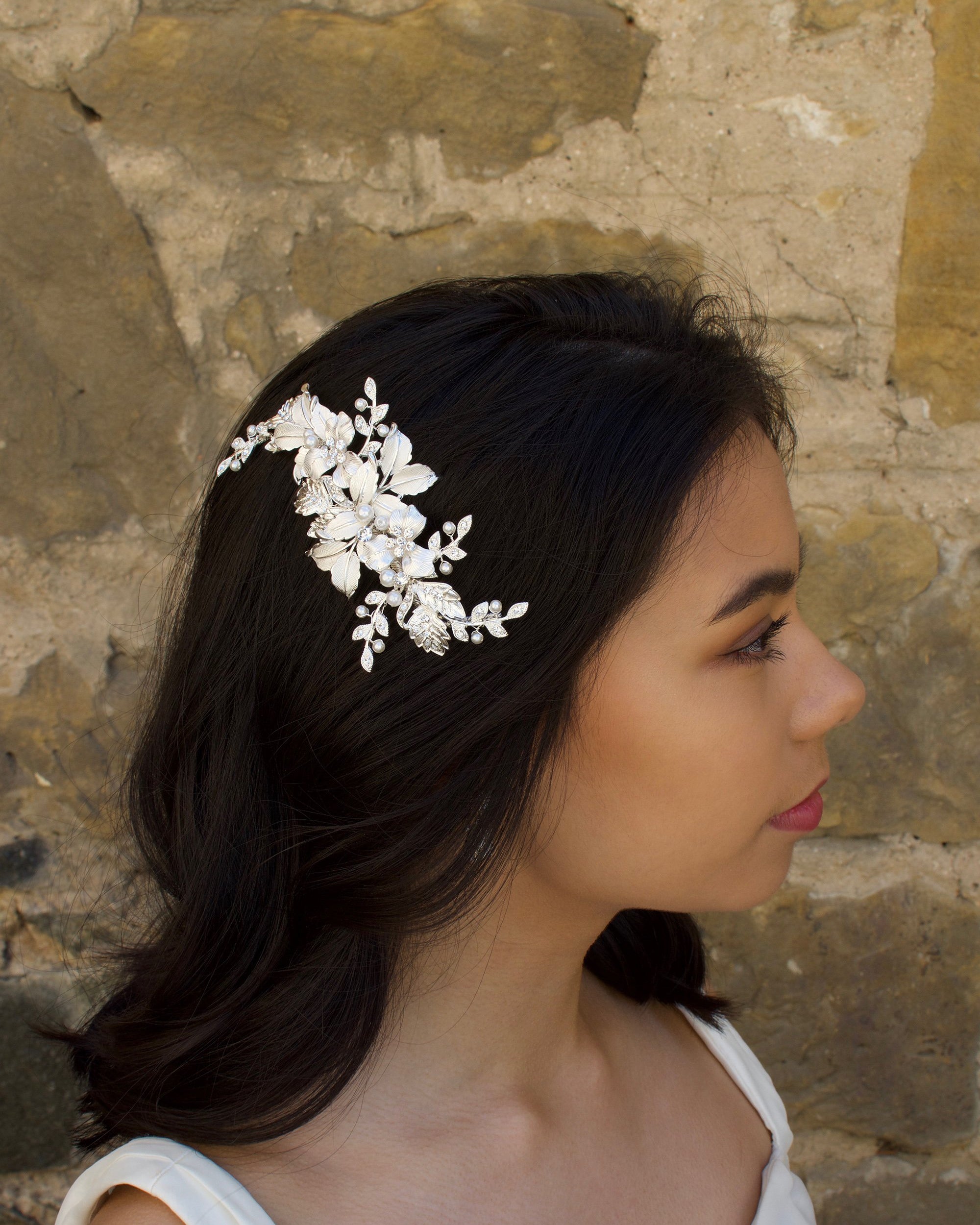 Soft Silver Side Comb with leaves and flowers worn by a dark hair bride with a stone wall backdrop