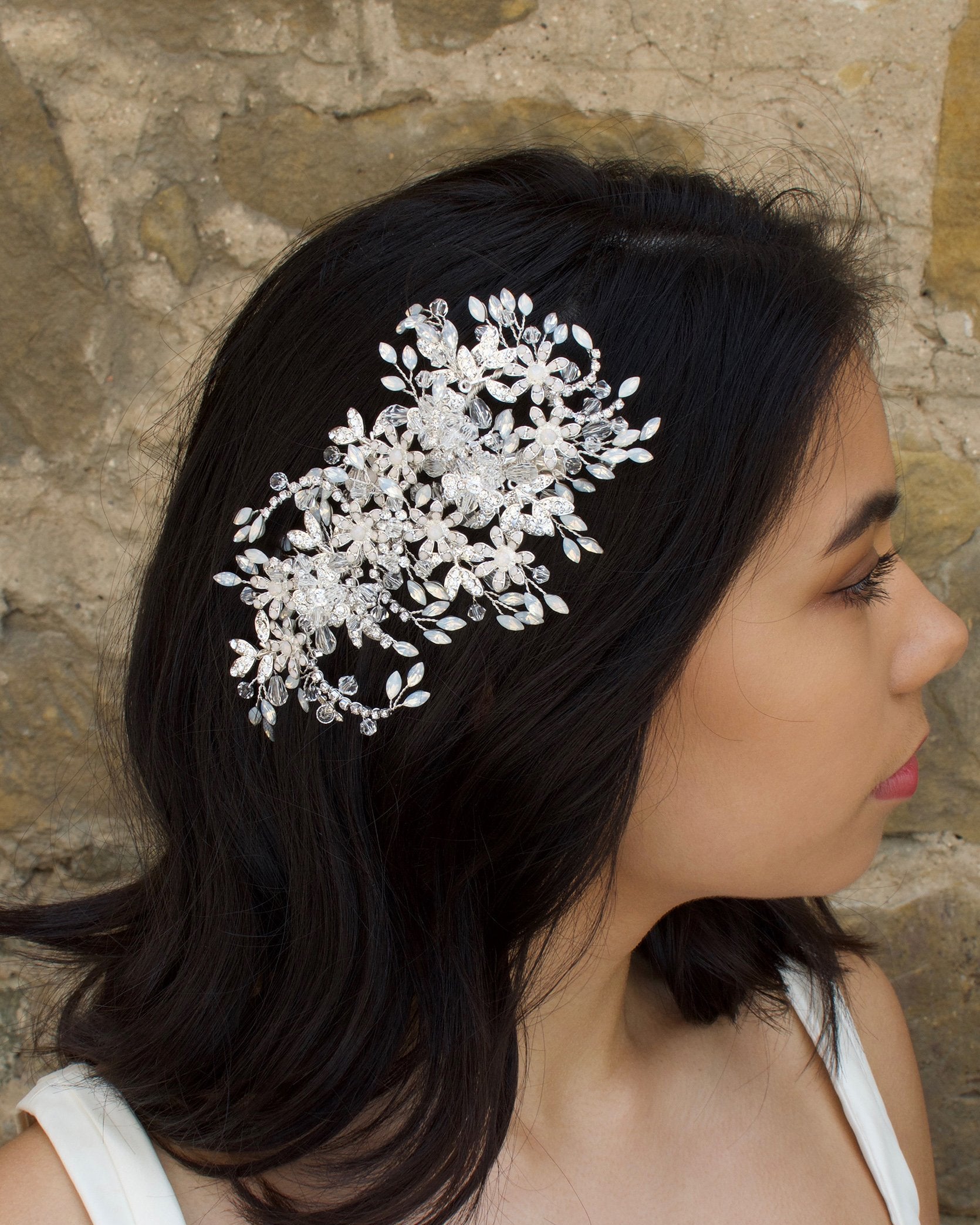 Model wears a large silver side comb on her dark hair with a stone wall background
