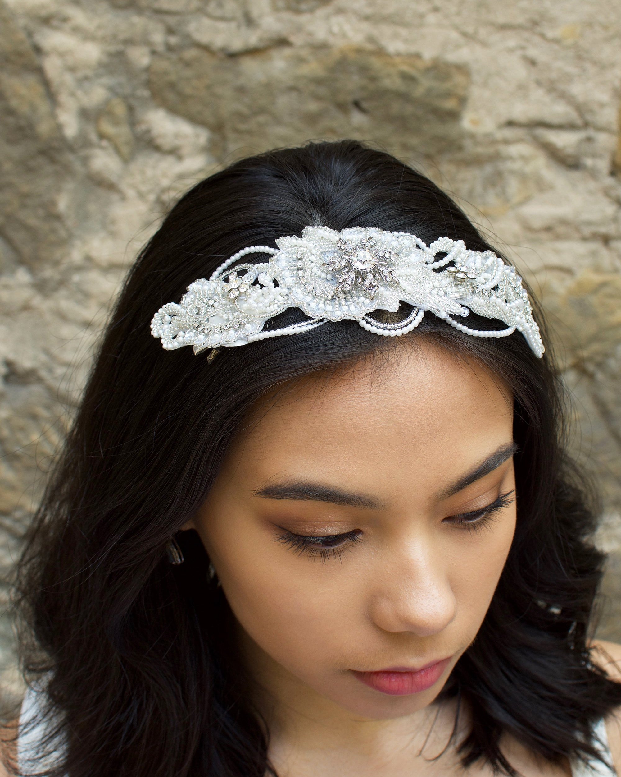 Dark Haired Bride wearing a seed pearl headpiece at the front on her black hair with a stone wall behind