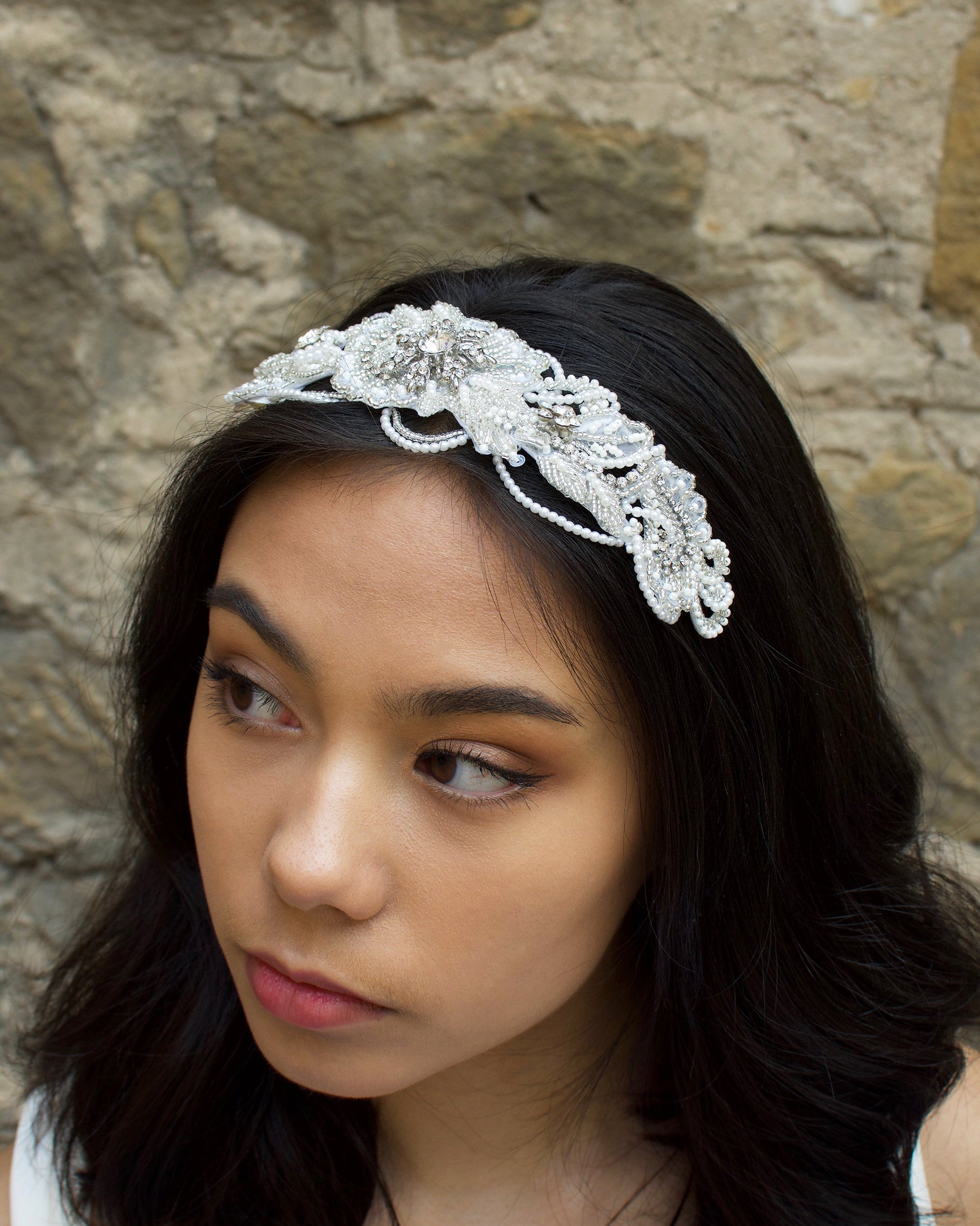 Bride with black hair wearing a seed pearl bridal comb at the front of her head with a stone wall background