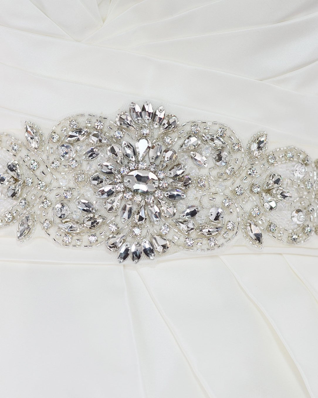 A wide bridal belt with crystals and beads worn on the waist of an ivory bridal gown with a white background