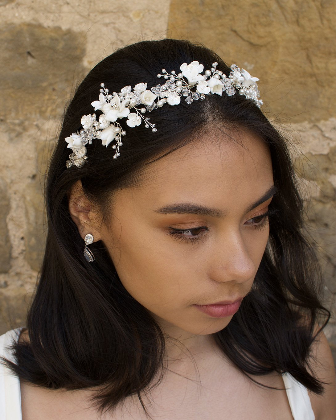 Dark hair model wears a headband of ceramic flowers and pearls with a wall background