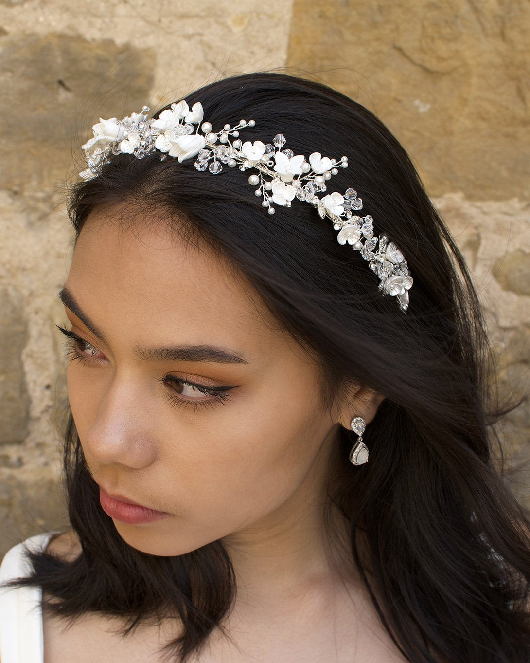 A bride with black hair wears a headband of ceramic flowers and clear crystals with a wall background