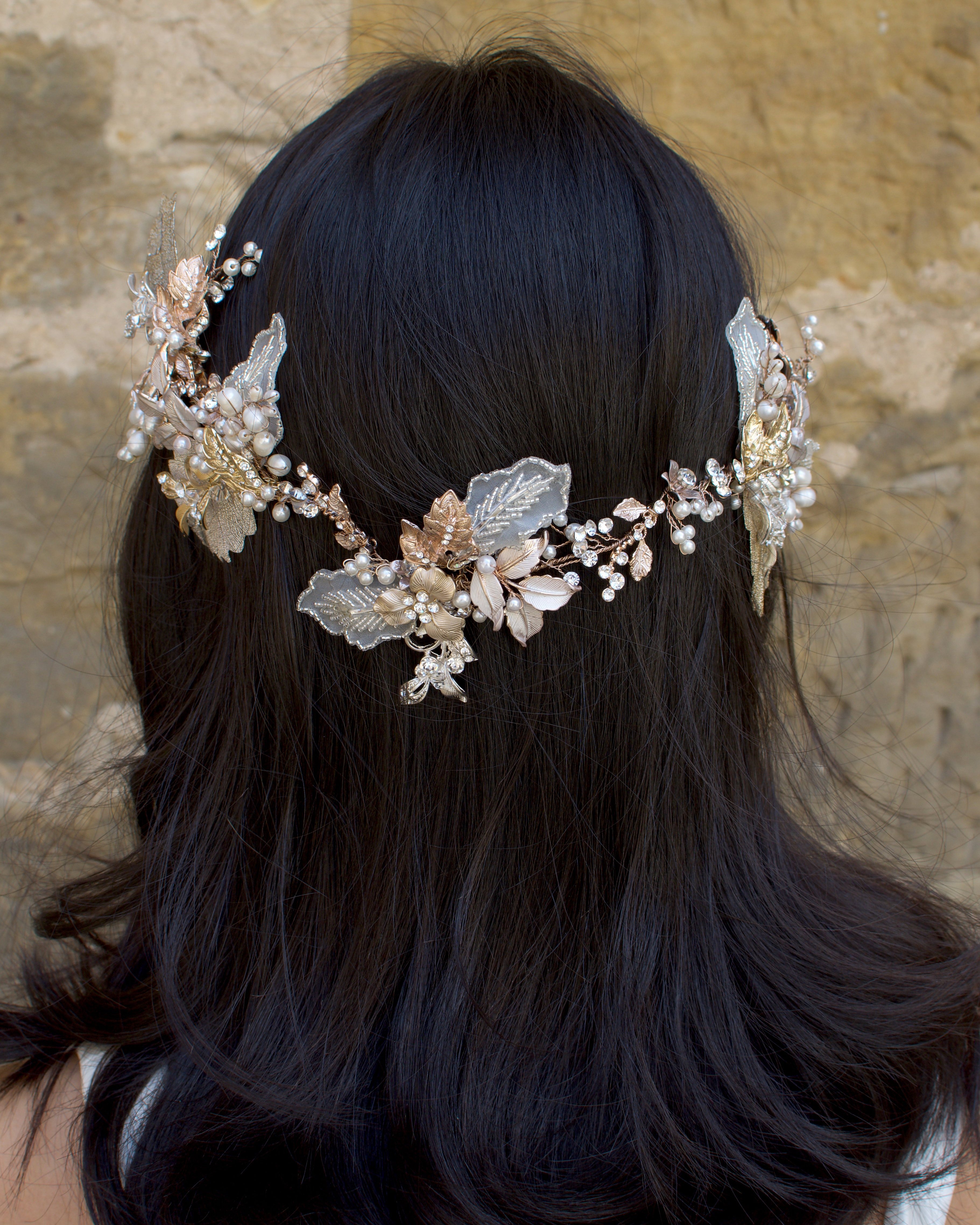 A dark haired model with hair down wears a Bridal Vine in Silver, Gold and Rose Gold with a background of a stone wall