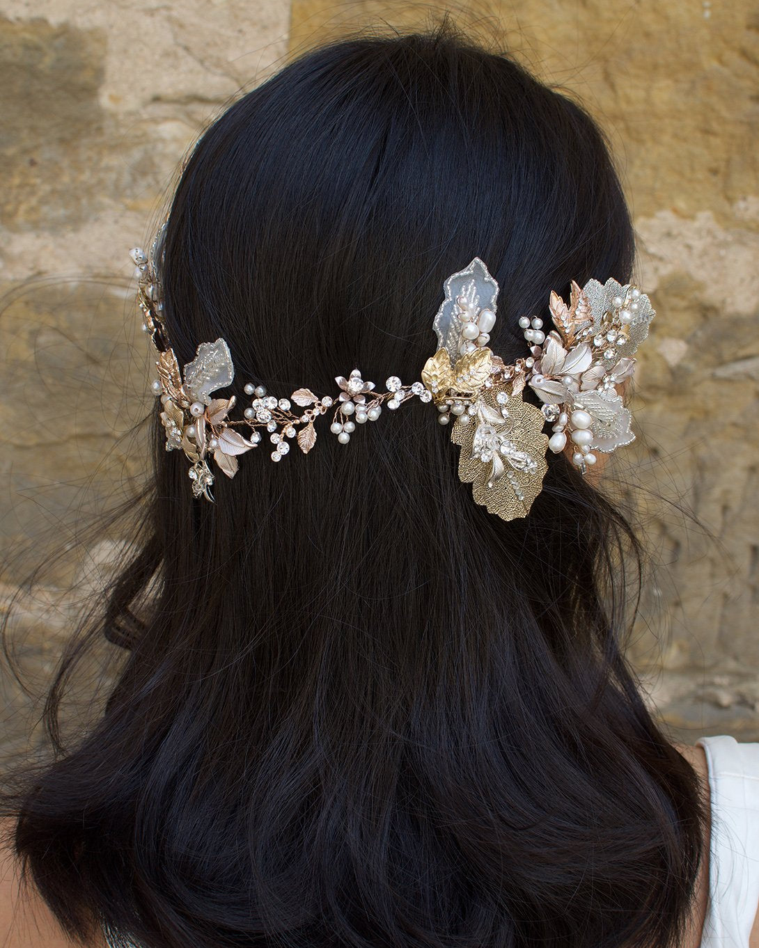A dark haired model wears a Bridal Vine in Silver, Gold and Rose Gold with a background of a stone wall