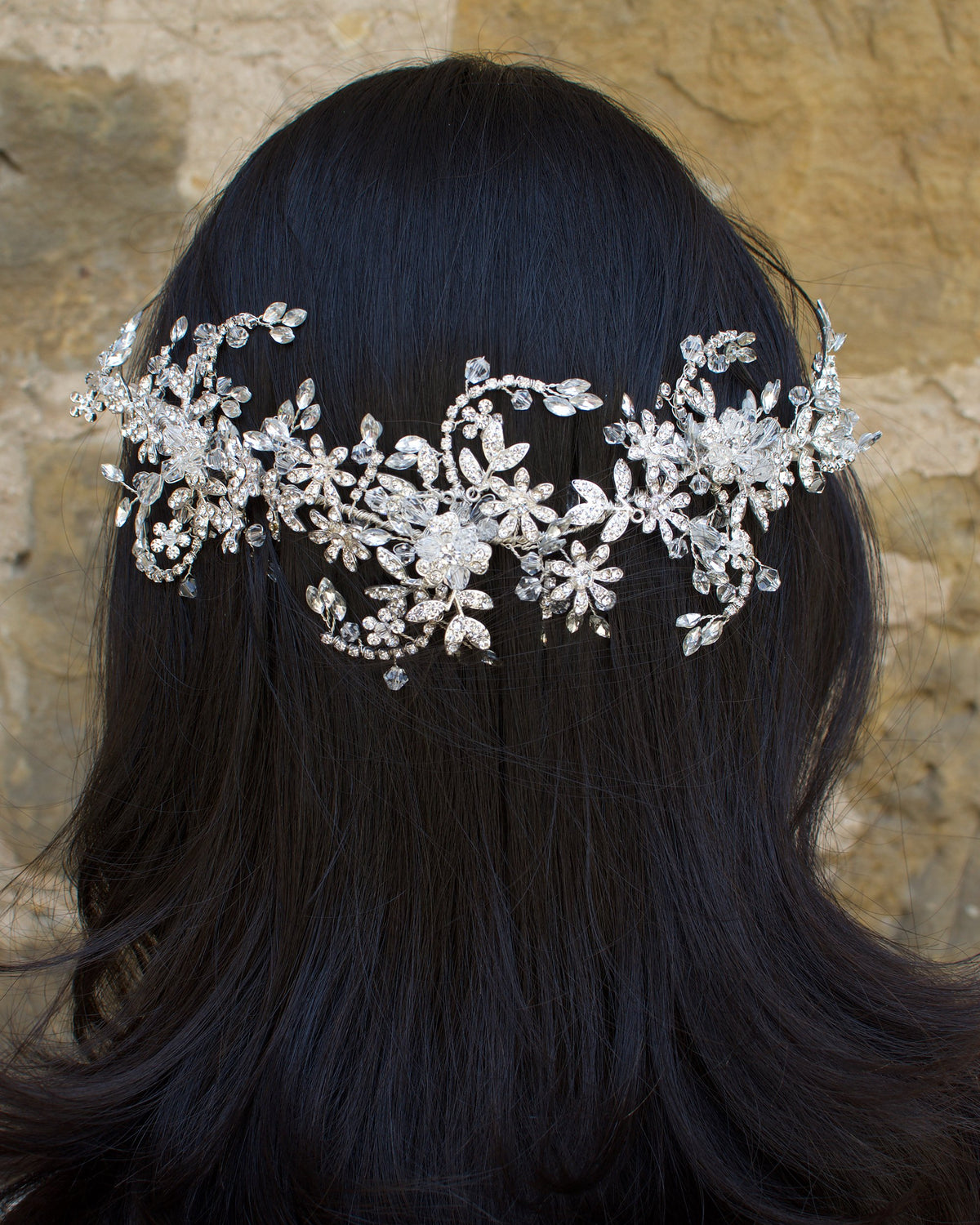 Silver and crystal headband worn at the back of a models head with a stone wall background